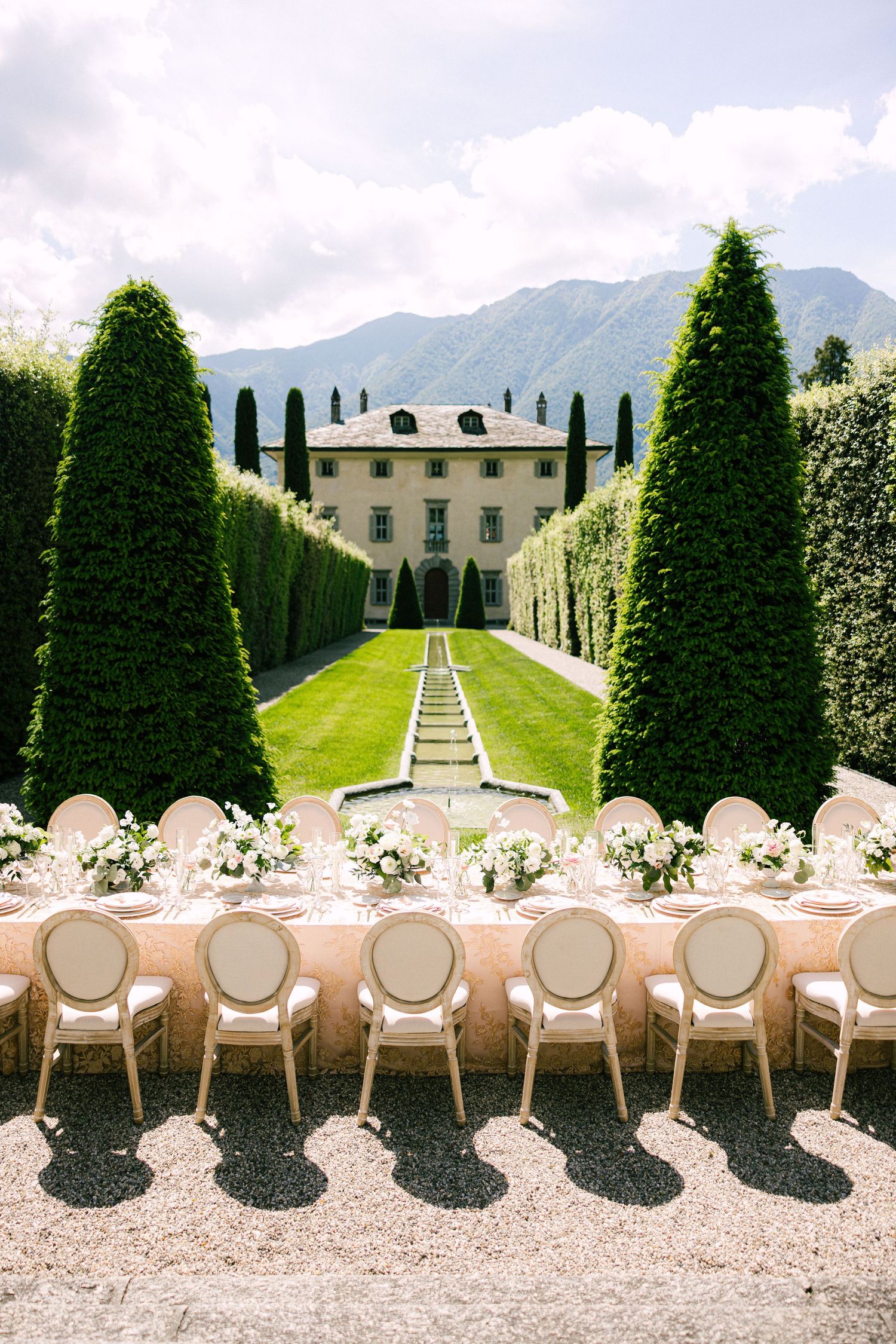 Aerial view of outdoor wedding reception at Italian villa with long banquet table, white chairs, and topiary trees.