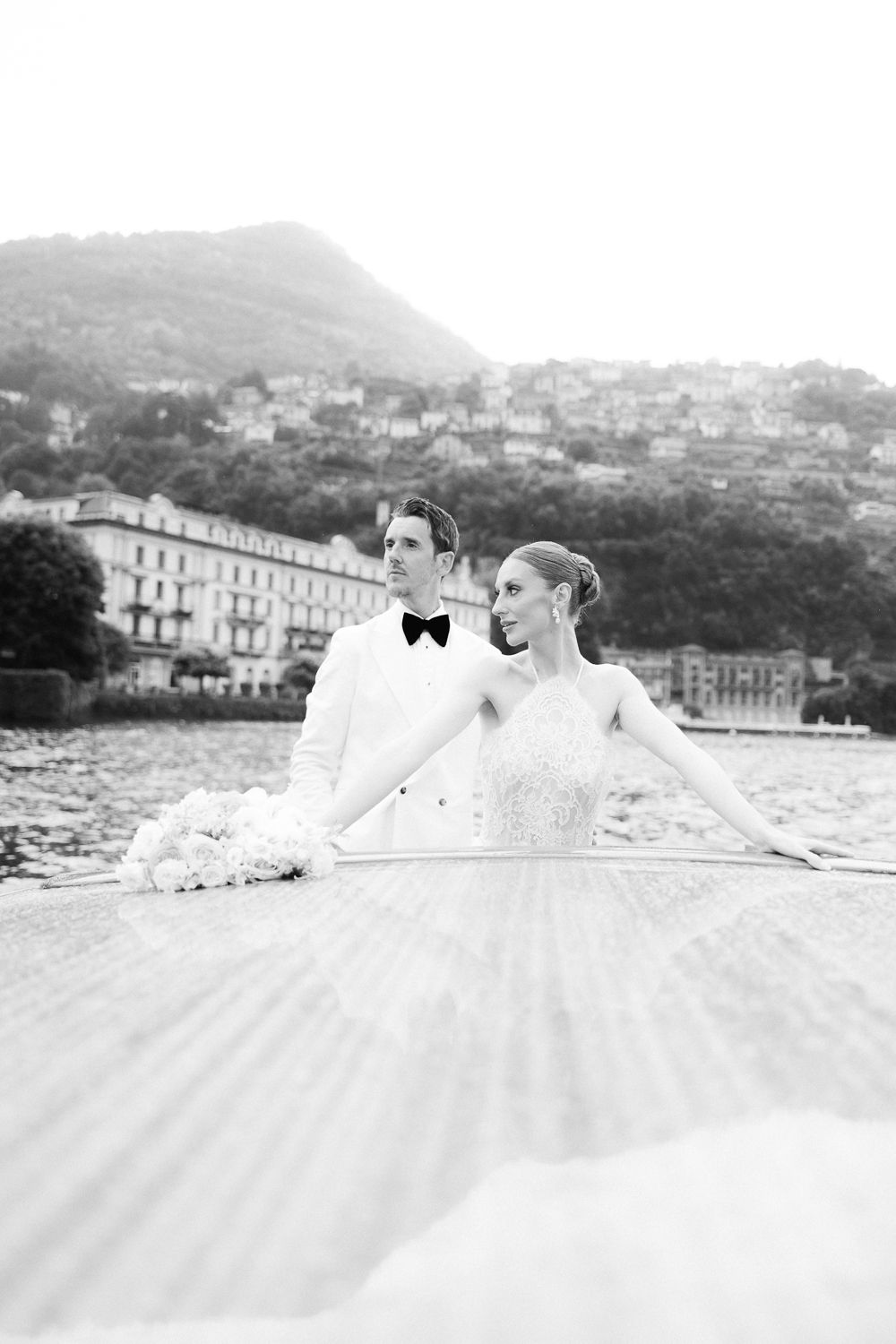 Black and white photo of bride and groom on boat deck with Lake Como village behind.