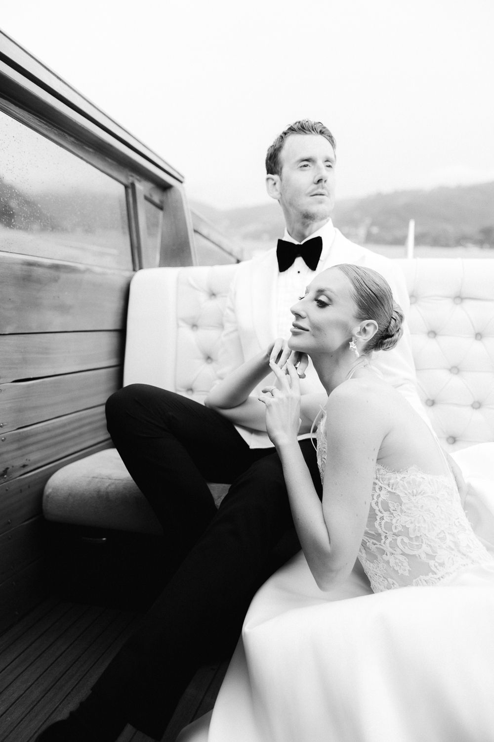 Black and white portrait of bride and groom seated on luxury wooden boat interior.