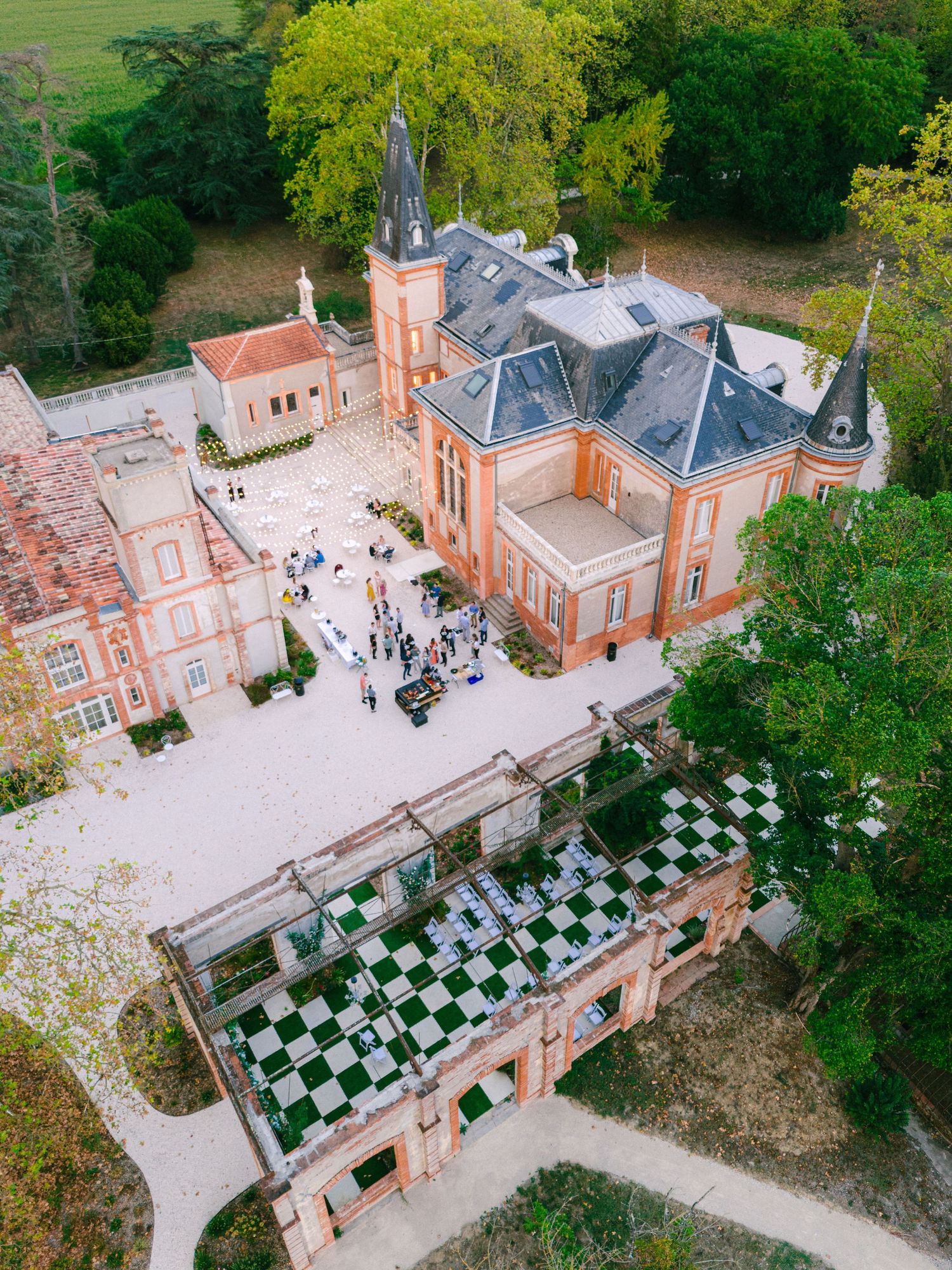 Aerial drone view of elegant French chateau wedding venue with checkered dance floor and lush surrounding gardens.
