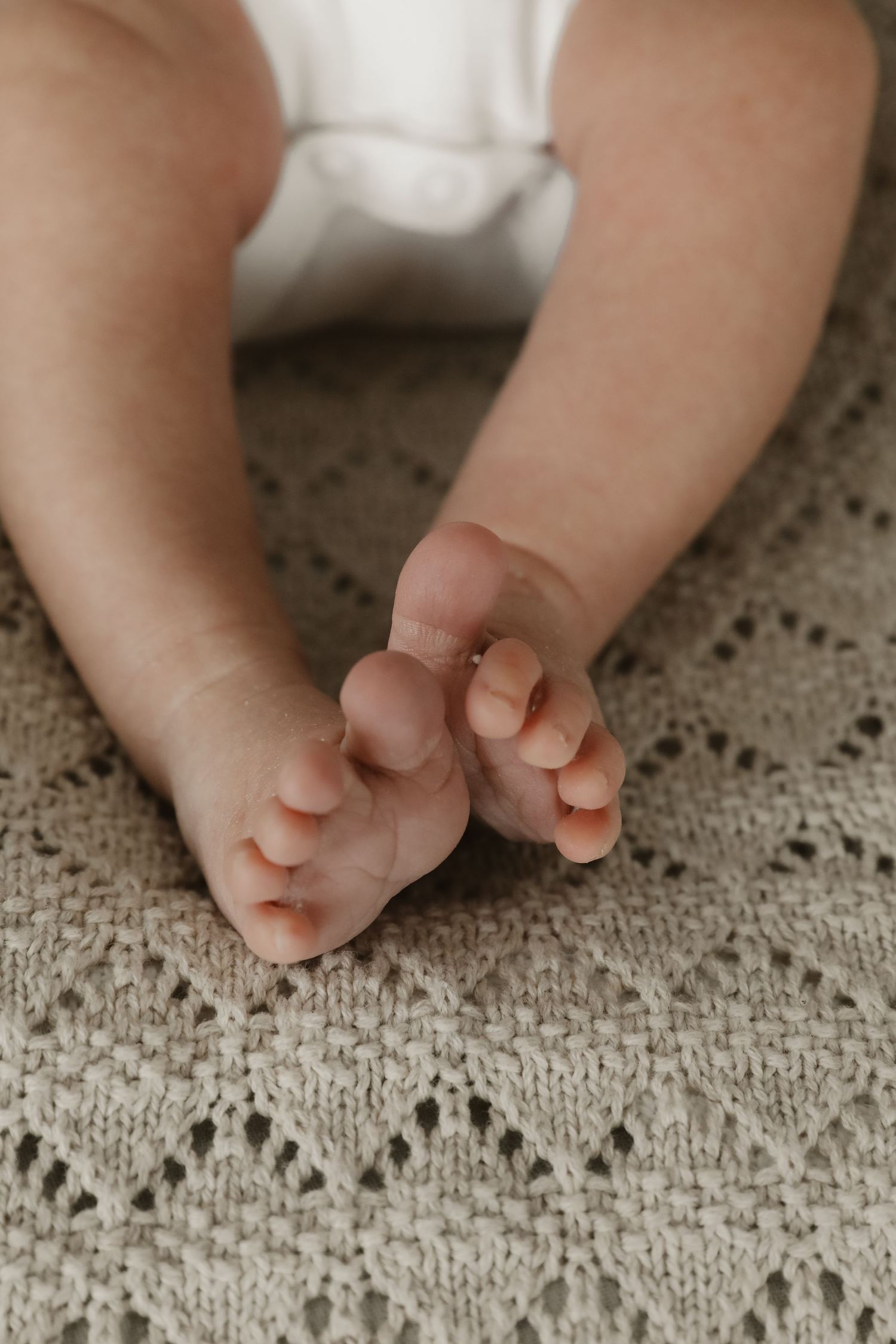 Close-up of tiny baby feet resting on a white crocheted blanket with delicate lace pattern.