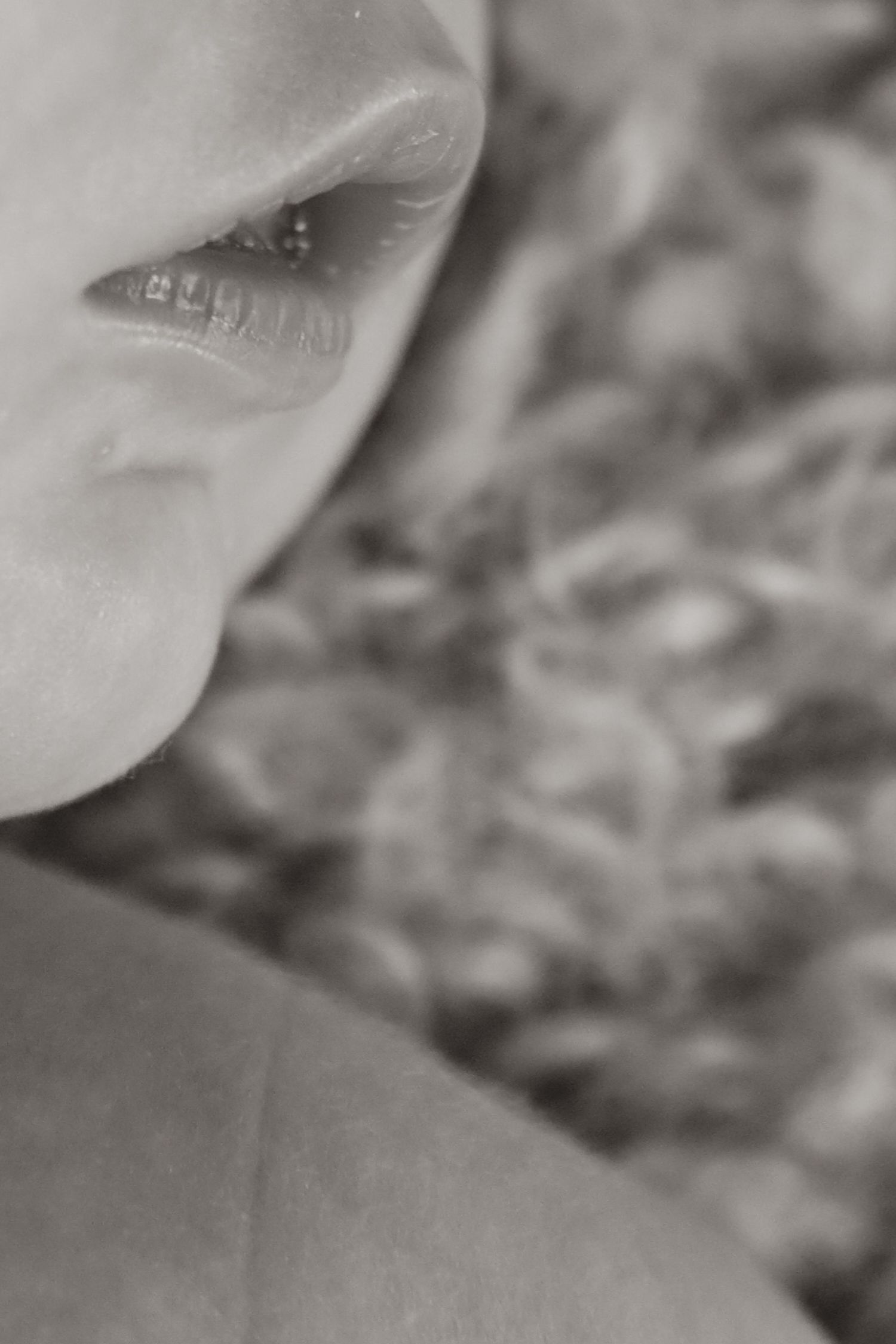 Close-up black and white photo of lips and skin in soft focus with blurred background.