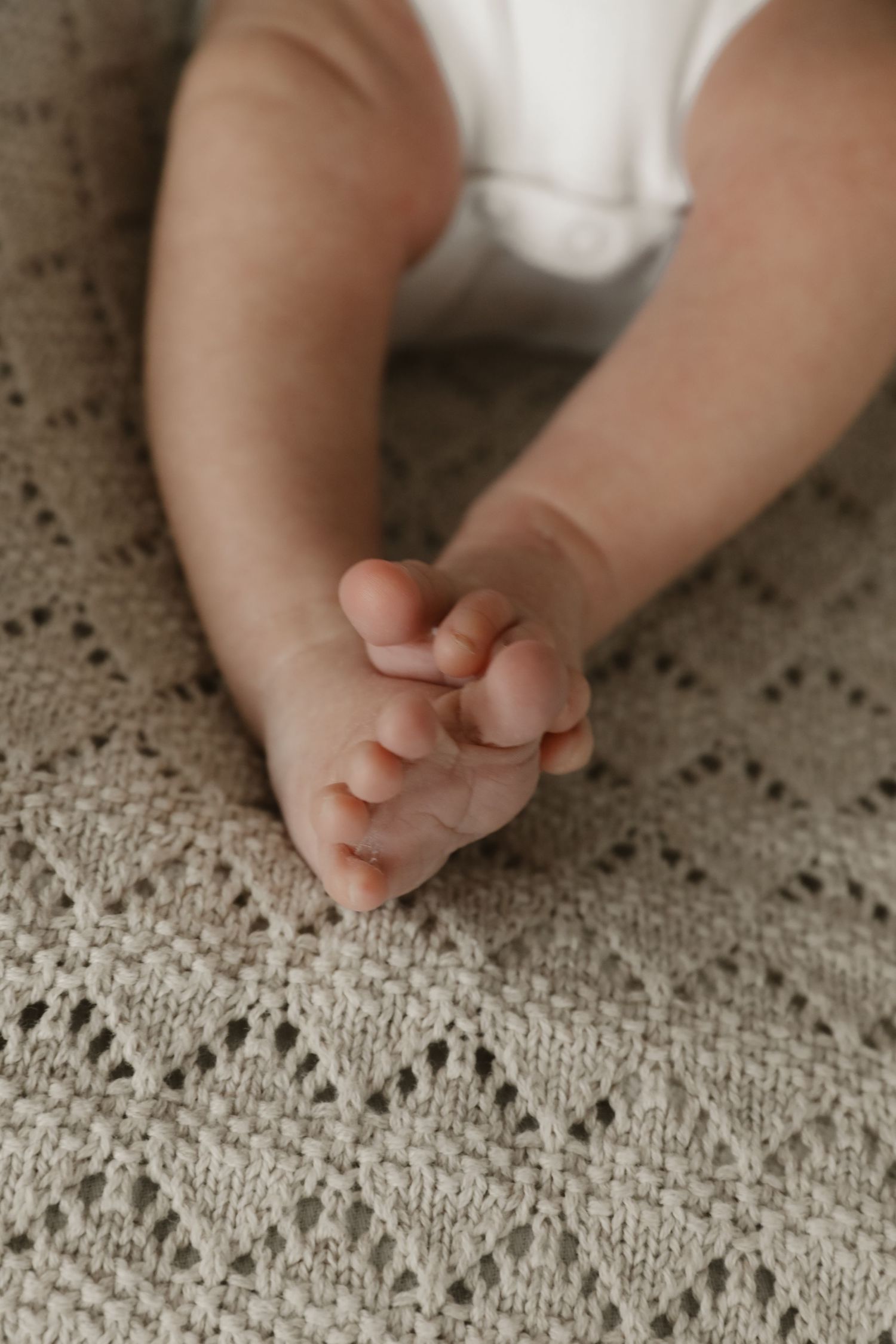 Close-up of tiny baby feet resting on a cream-colored knit blanket with delicate lace pattern.