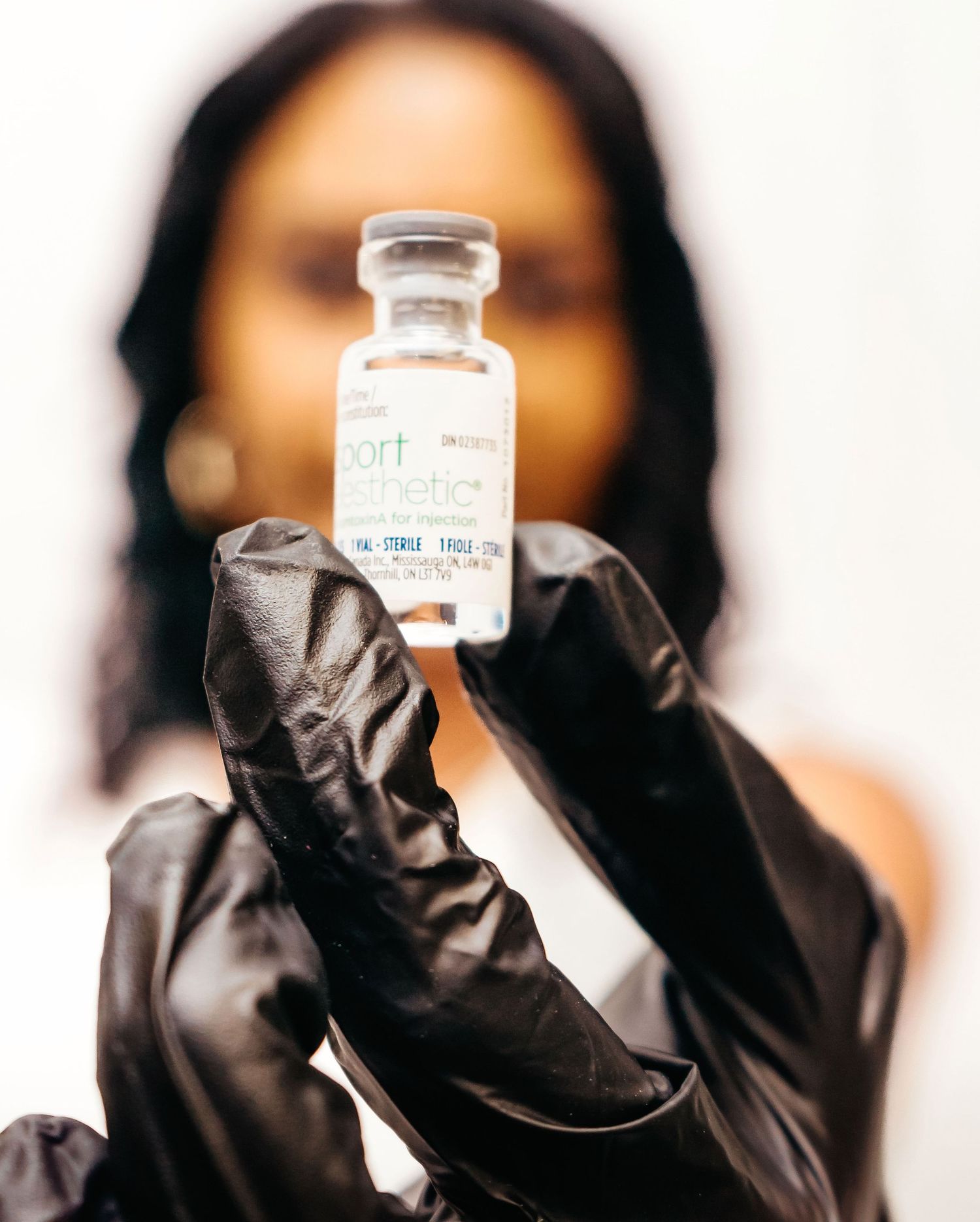 A gloved hand holds up a clear medical vial containing vaccine against a blurred background.