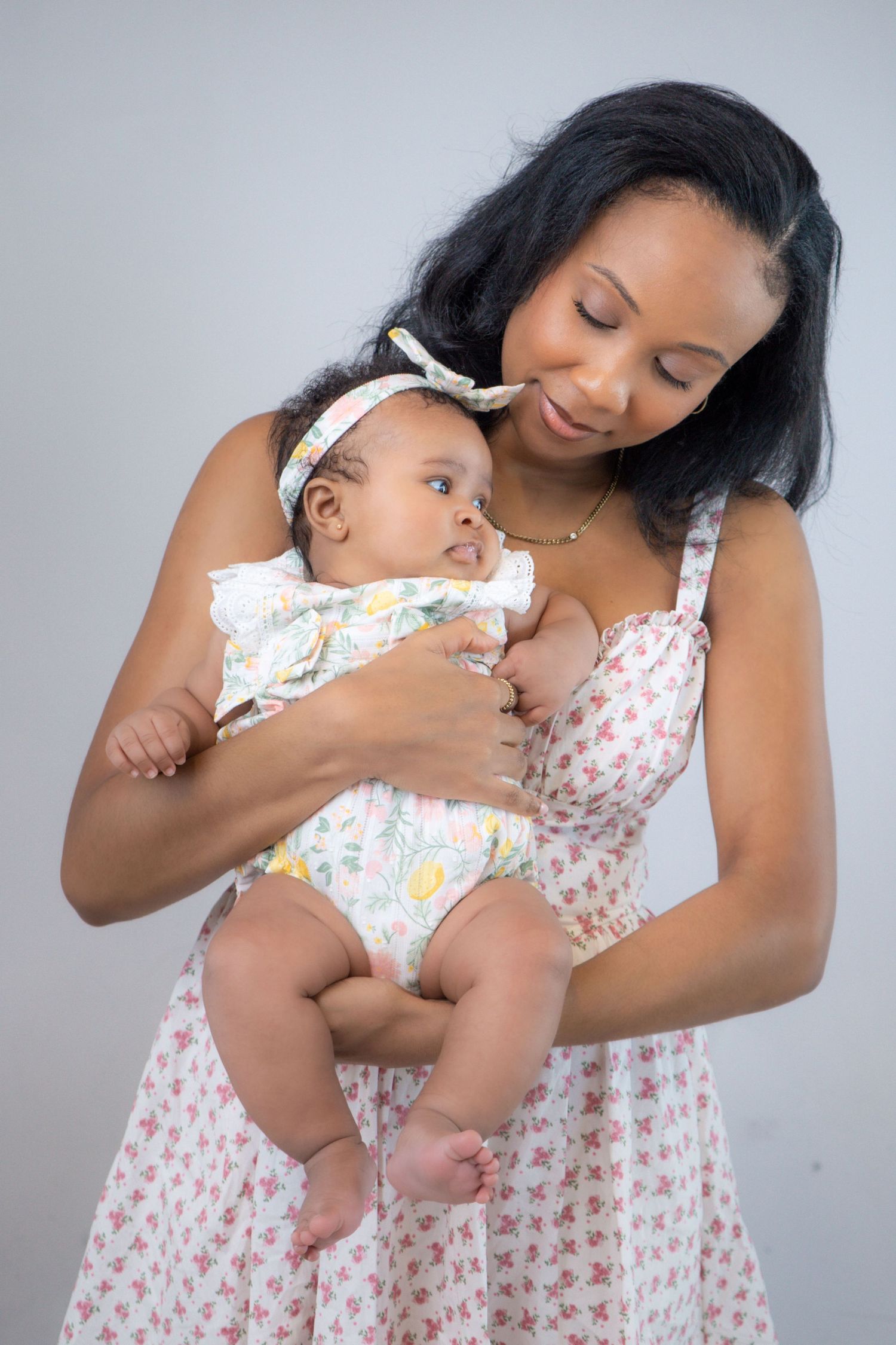 A tender moment between parent and baby wearing matching floral patterns against a light gray background.