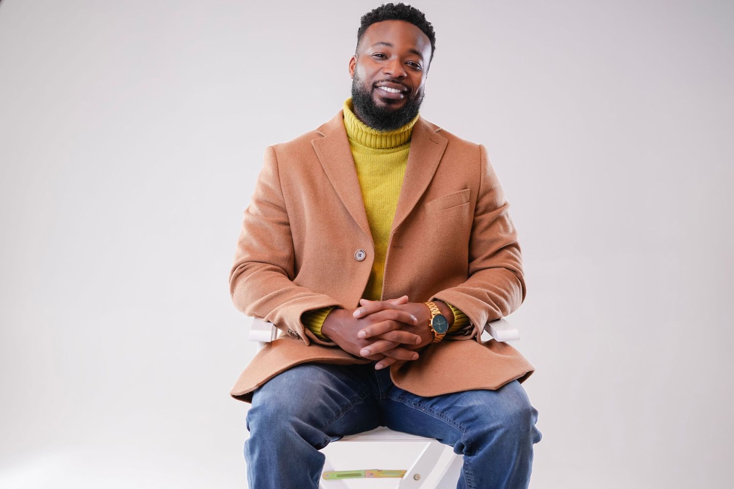 A person in a peach blazer and yellow turtleneck sits confidently against a white background.