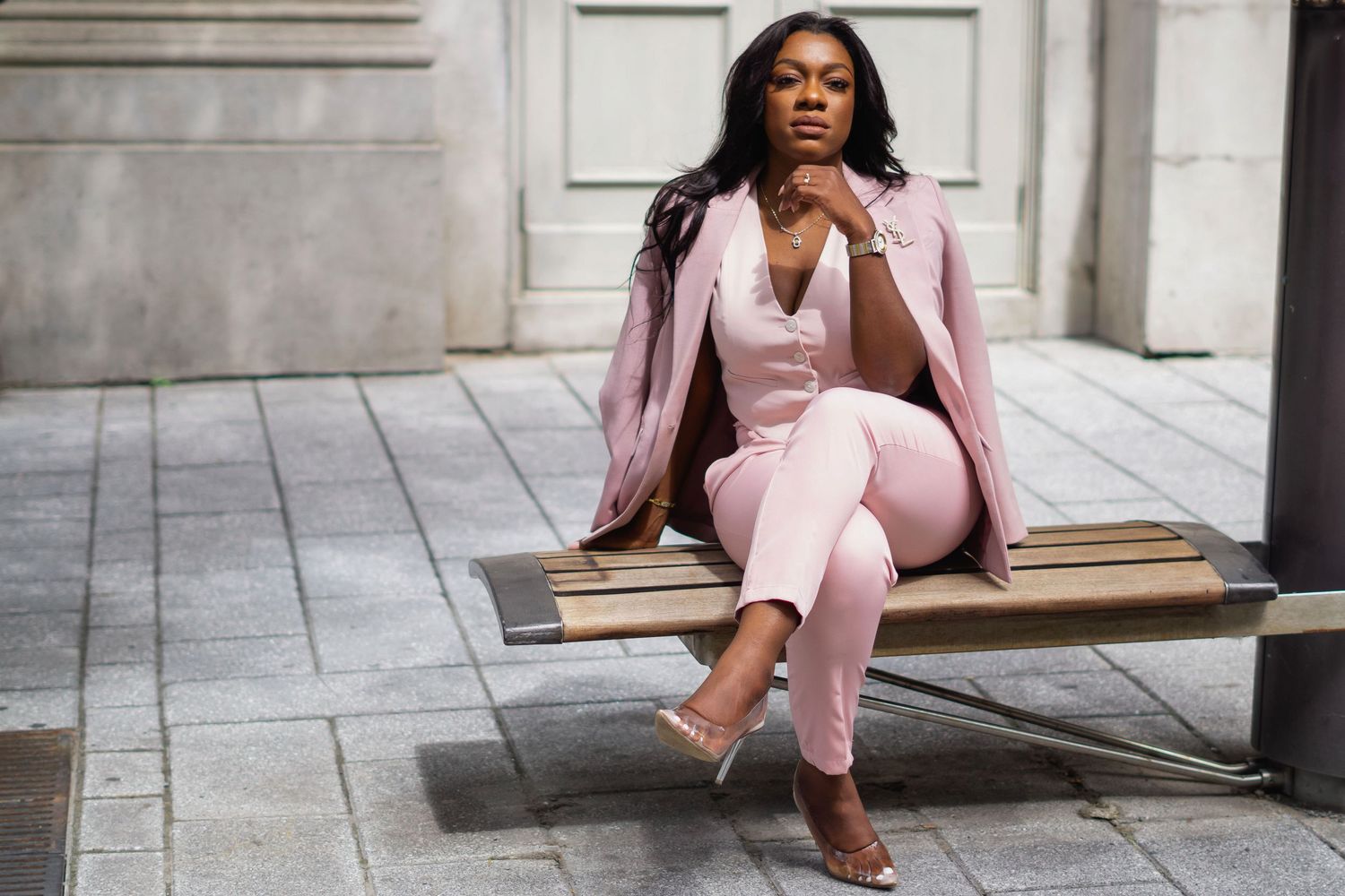 Professional woman in a stylish pink business suit sits confidently on stone steps in an urban setting.