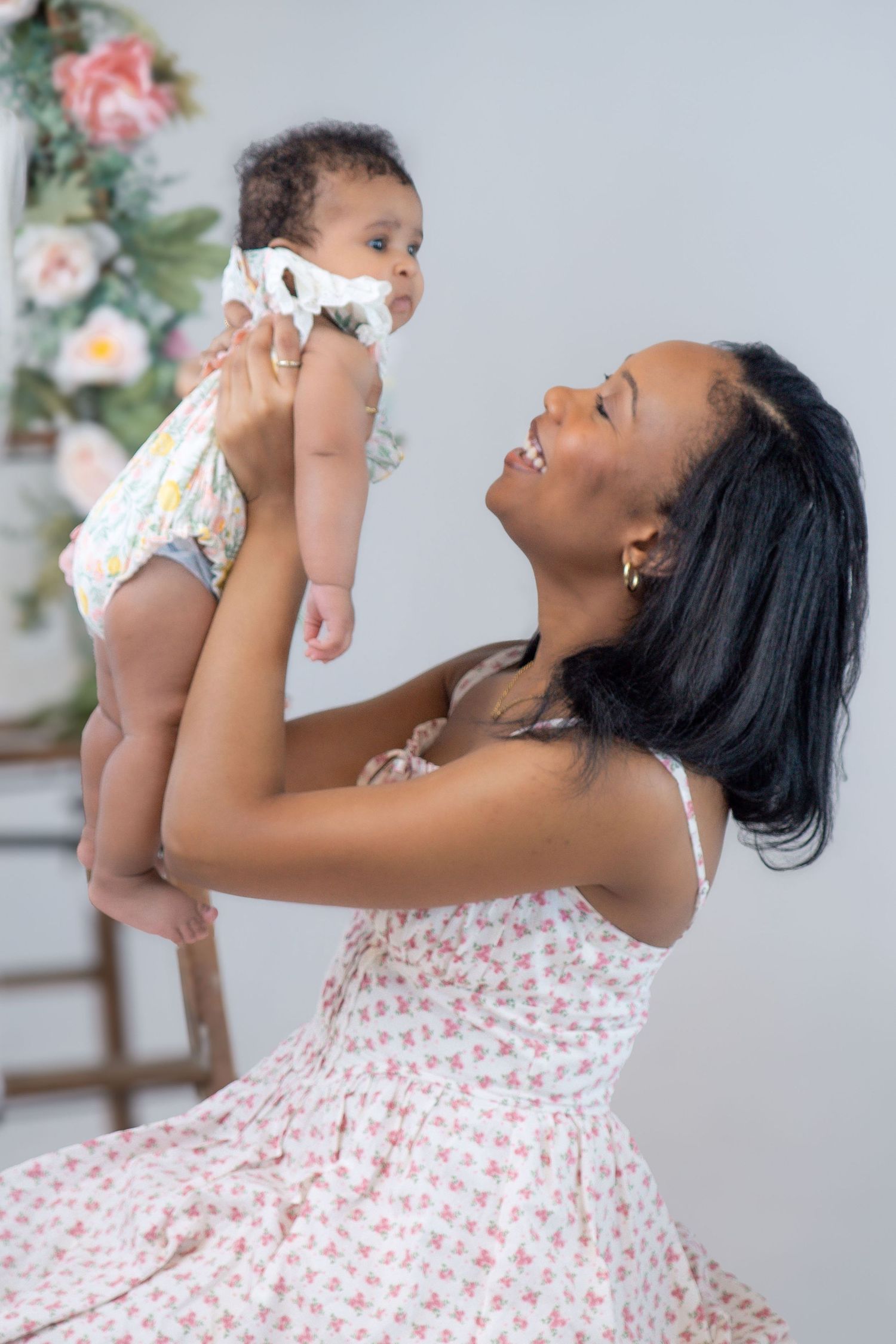 A tender moment between parent and baby wearing floral print dress against a white background.