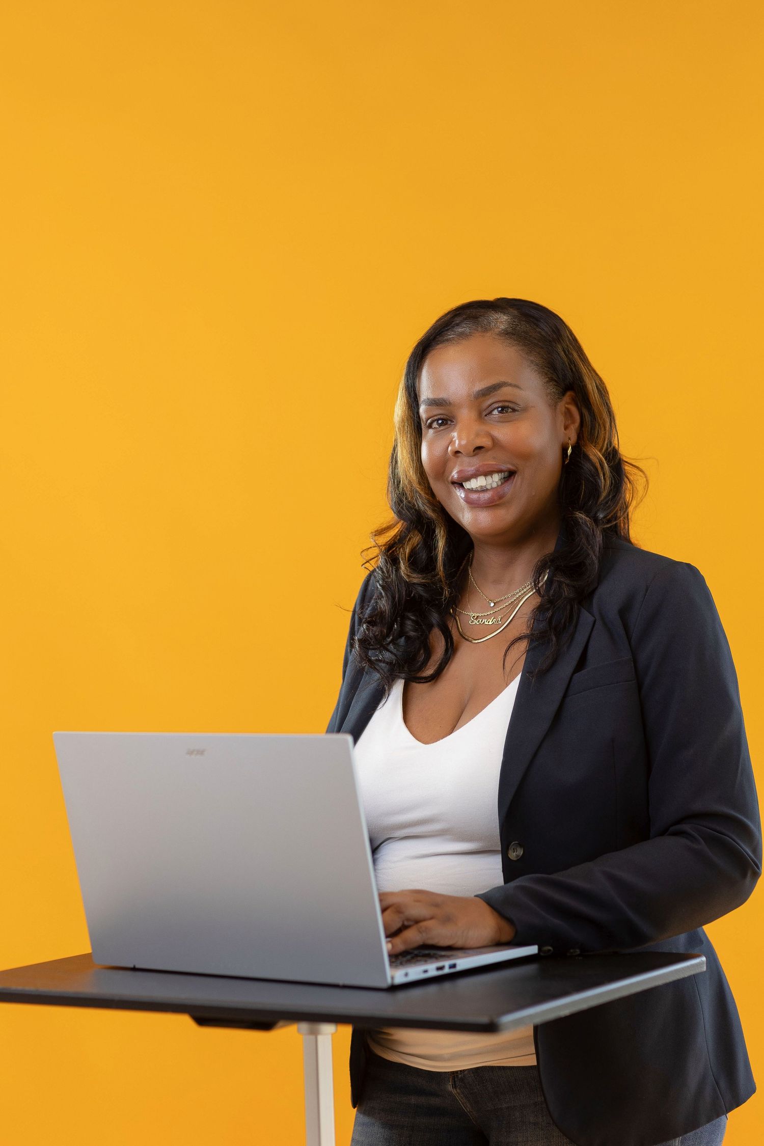 Professional in business attire works on laptop computer against vibrant orange background in studio setting.