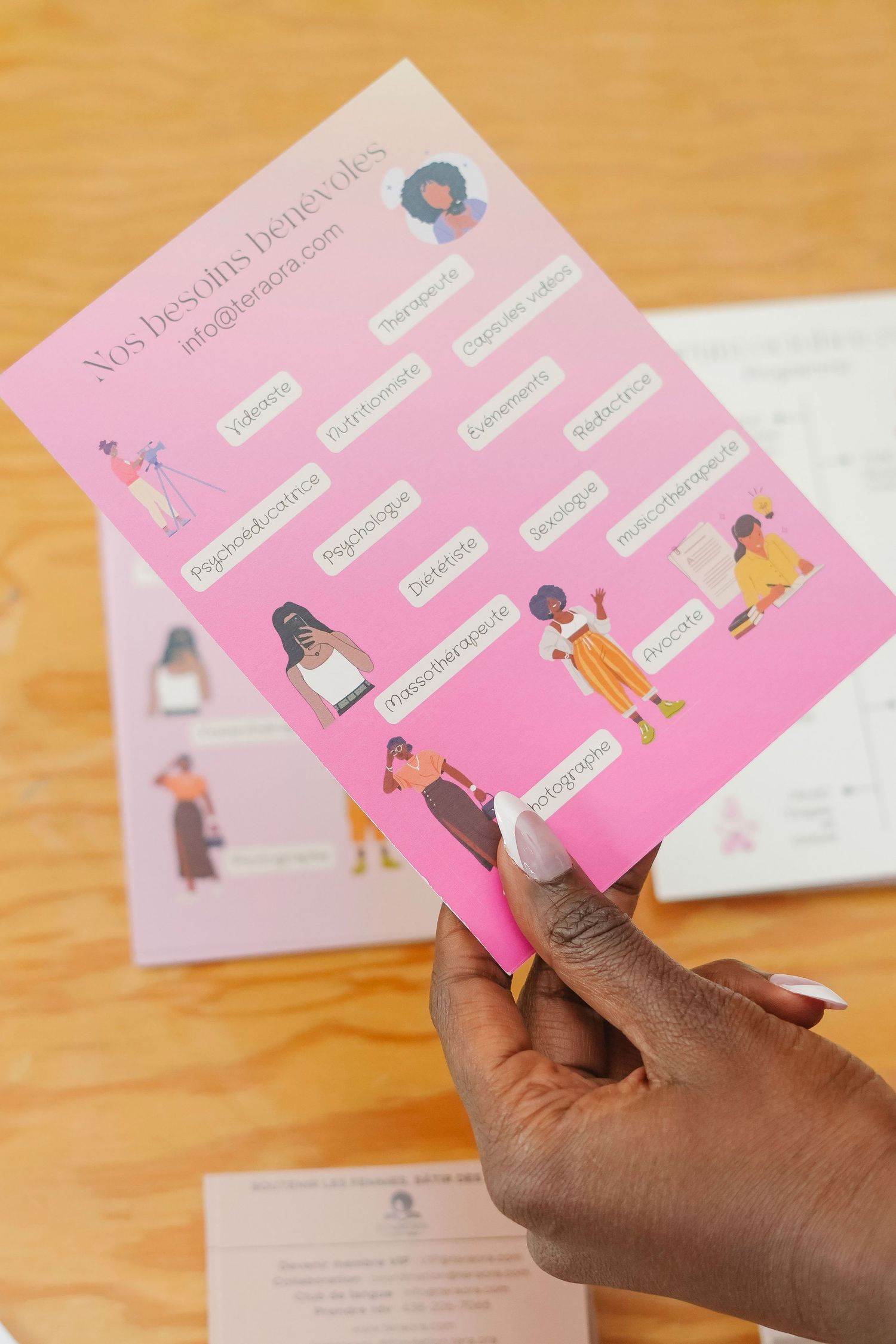 A hand holds a pink health information card with illustrated figures and text on a wooden surface.