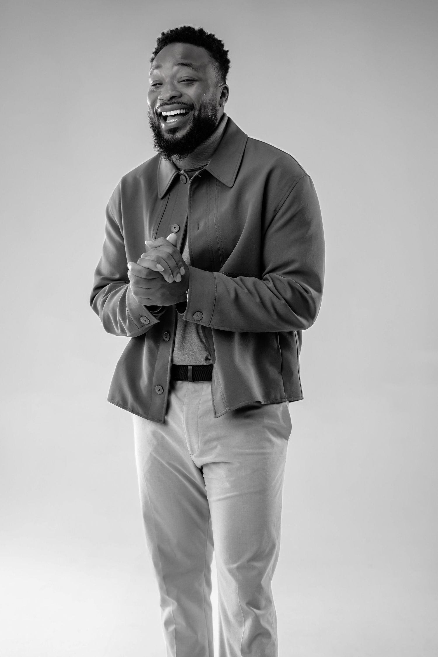 A person in a dark jacket and light pants laughs joyfully in a black and white photo series.