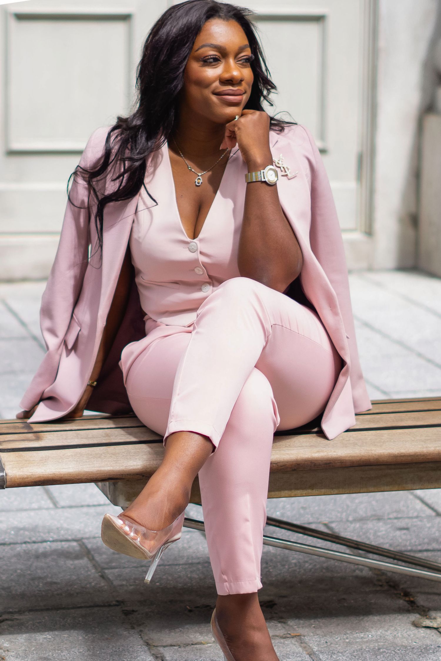 Professional portrait of someone wearing a chic pink business suit and clear heels while sitting elegantly on stone steps.