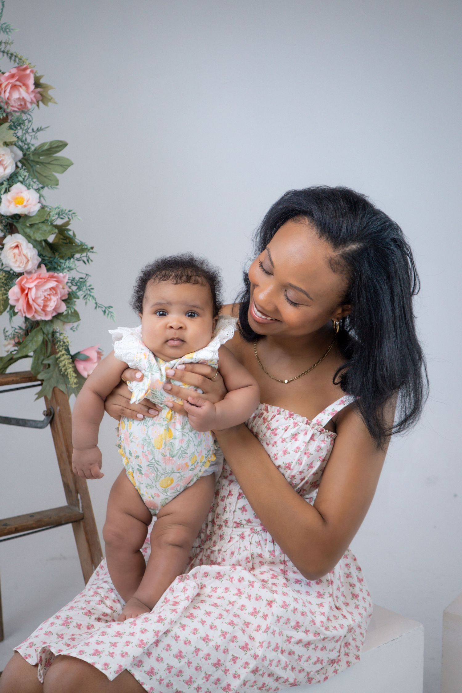 A tender moment between parent and baby against a floral backdrop in a light studio setting.