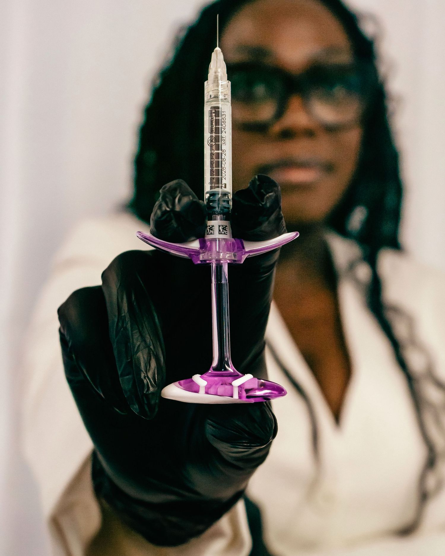 Four sequential images showing hands in black gloves holding a syringe against a light background.