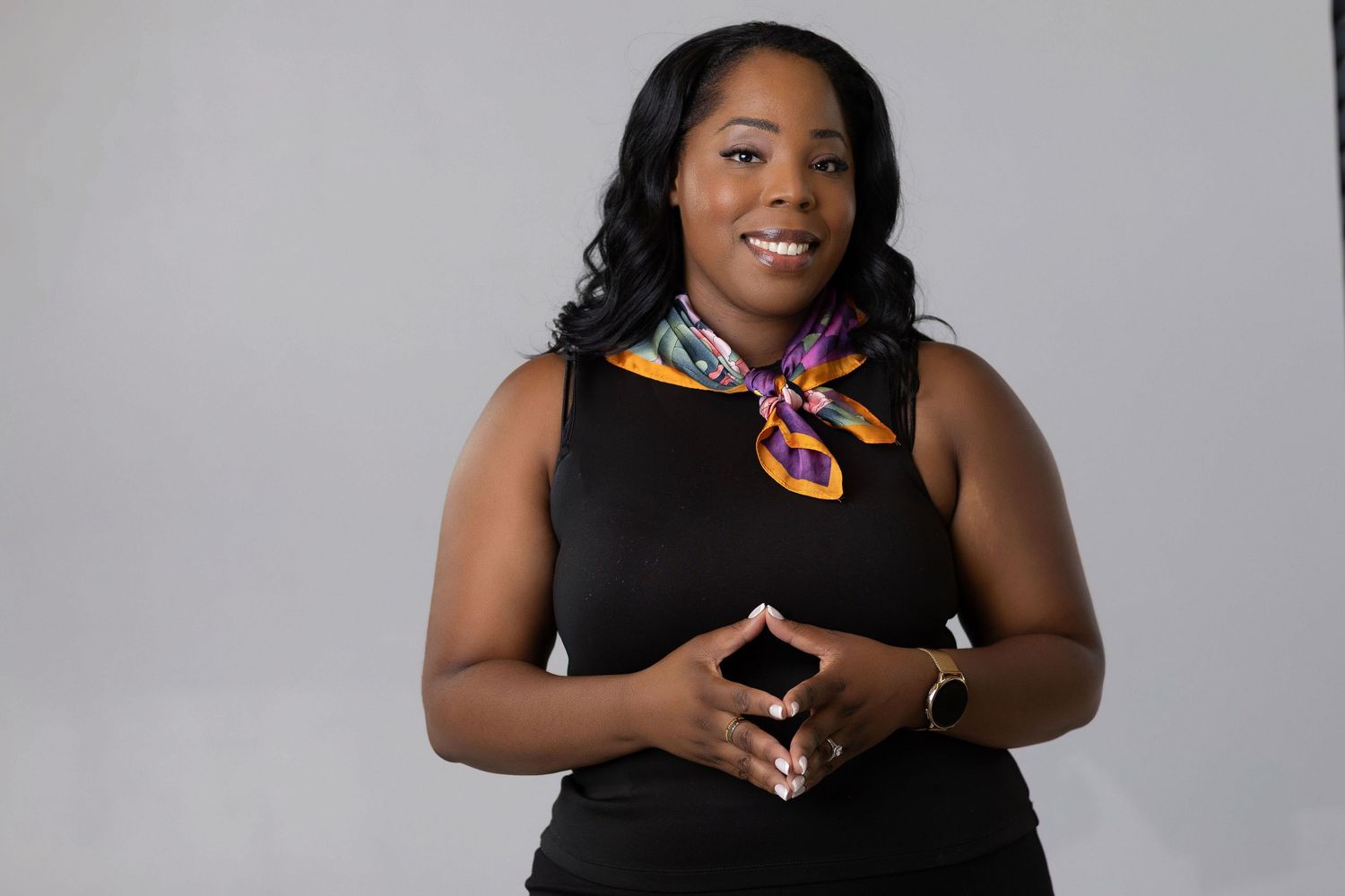 Professional portrait of a woman in a black sleeveless top with a colorful silk scarf and bright smile.