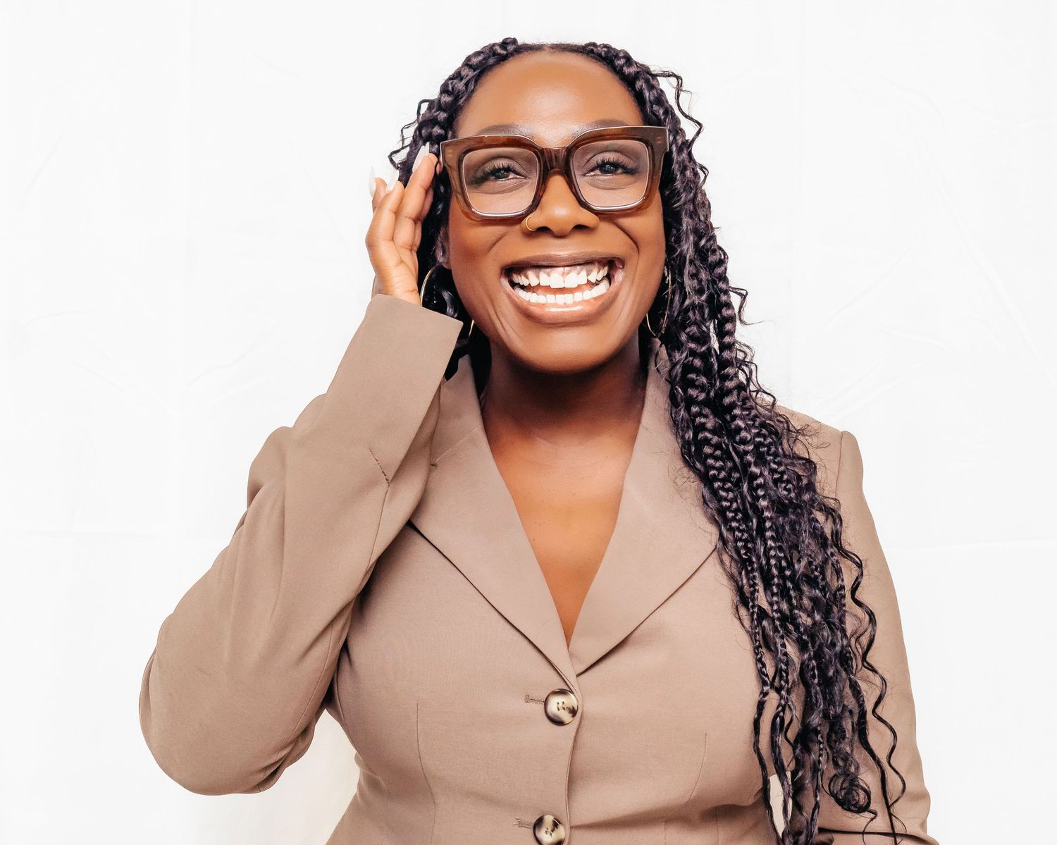Professional wearing glasses and a beige blazer smiles warmly against white background.