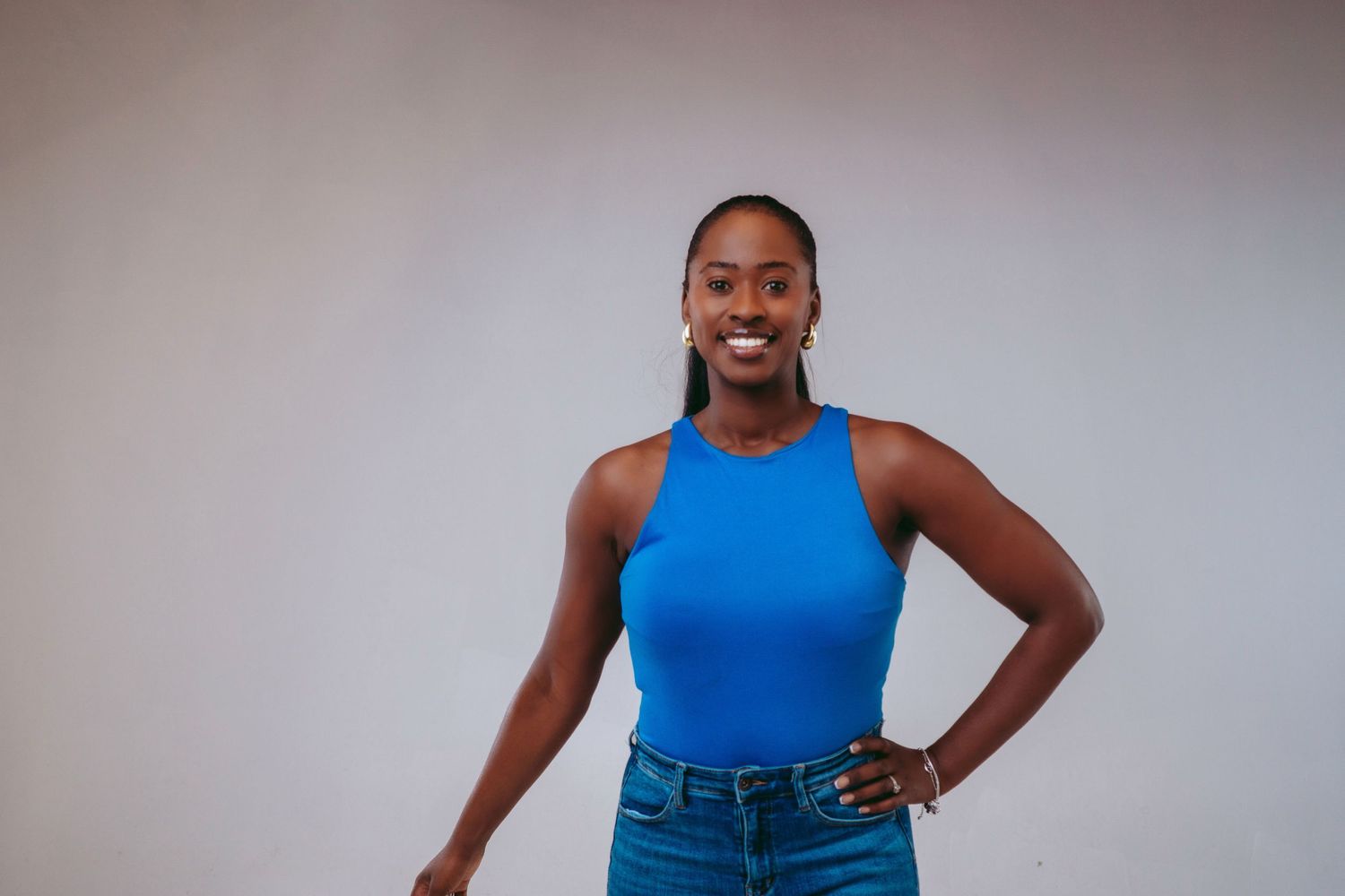 Person in bright blue sleeveless top and jeans poses confidently against a light background.