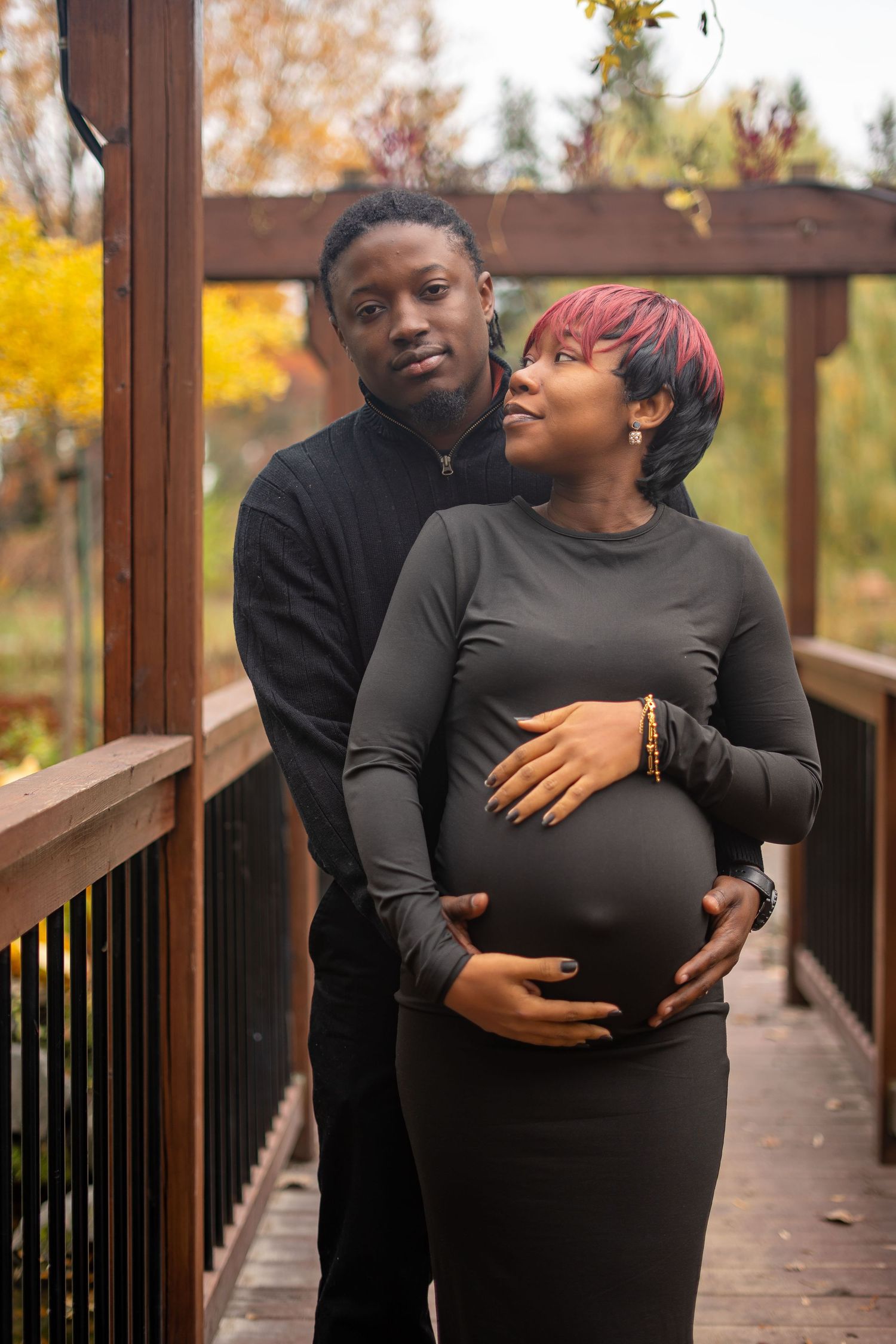 A couple shares a tender moment on a wooden bridge surrounded by autumn foliage.