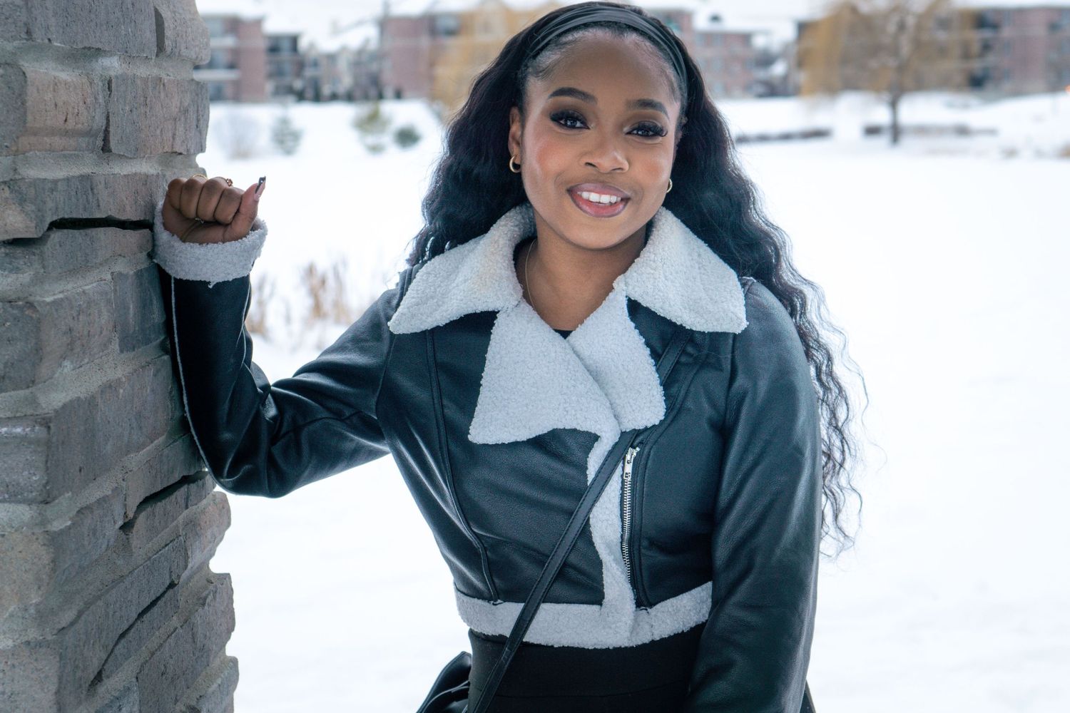 Fashion portrait in black leather jacket against snowy urban backdrop.