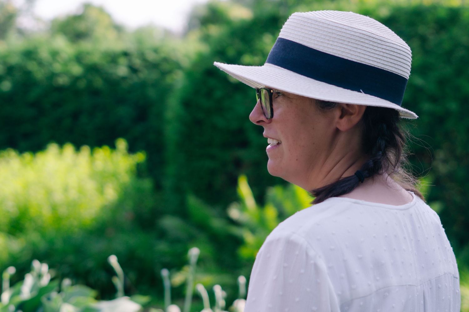 A person in a white sun hat and shirt enjoys a sunny day in a lush garden setting.