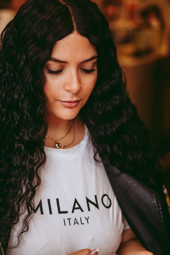 Person wearing white Milano Italy t-shirt with dark curly hair in warm lighting.
