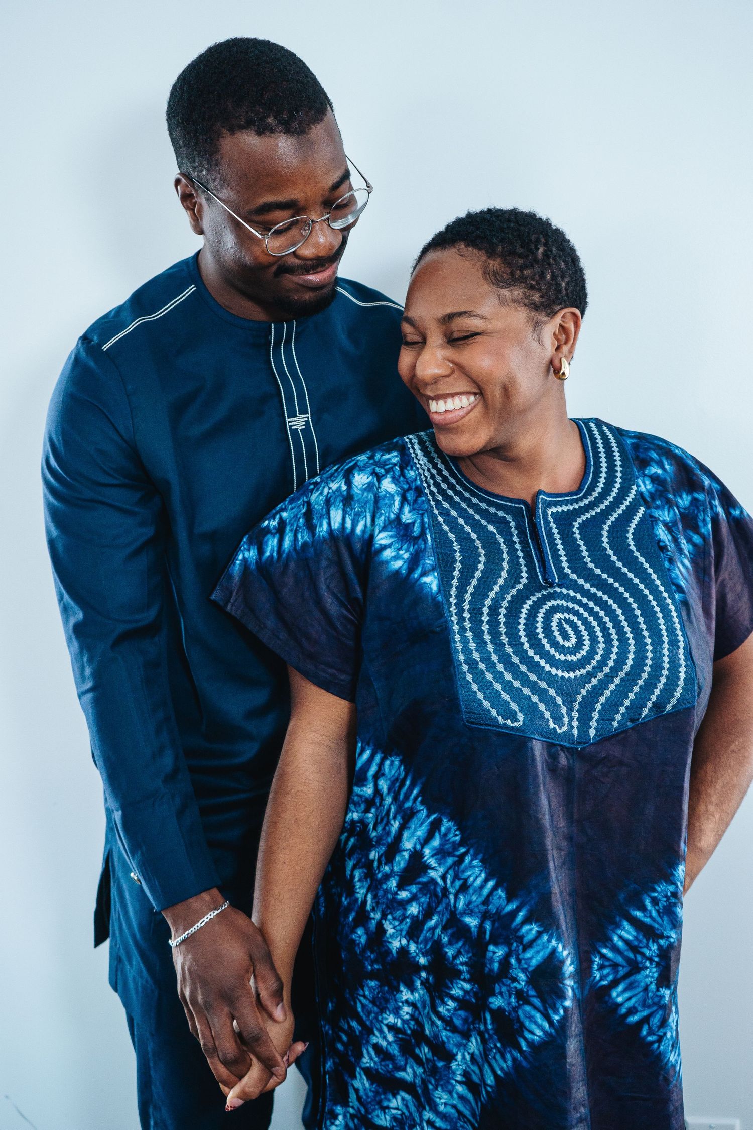 A couple wearing coordinated blue African print outfits share an intimate moment against a white background.