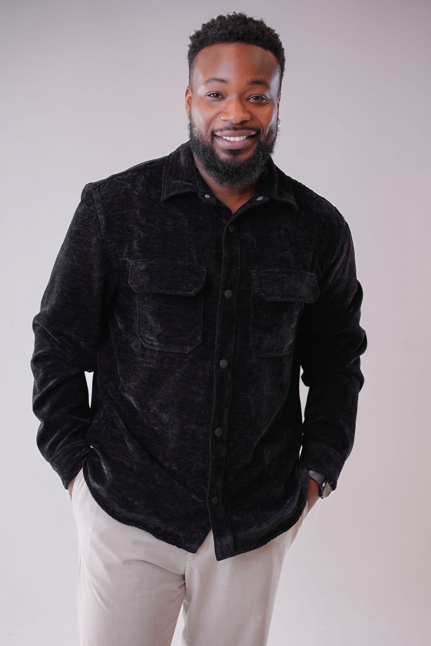 A person wearing a black corduroy jacket and light colored pants poses against a white background.
