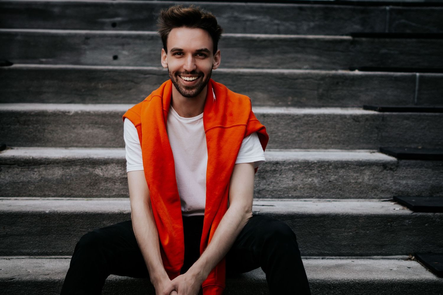 A series of photos showing someone in a bright orange vest sitting on concrete steps against a dark background.