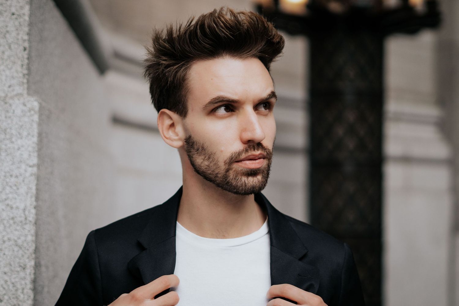 Professional portrait of person in black suit jacket looking to the side with thoughtful expression in modern setting.