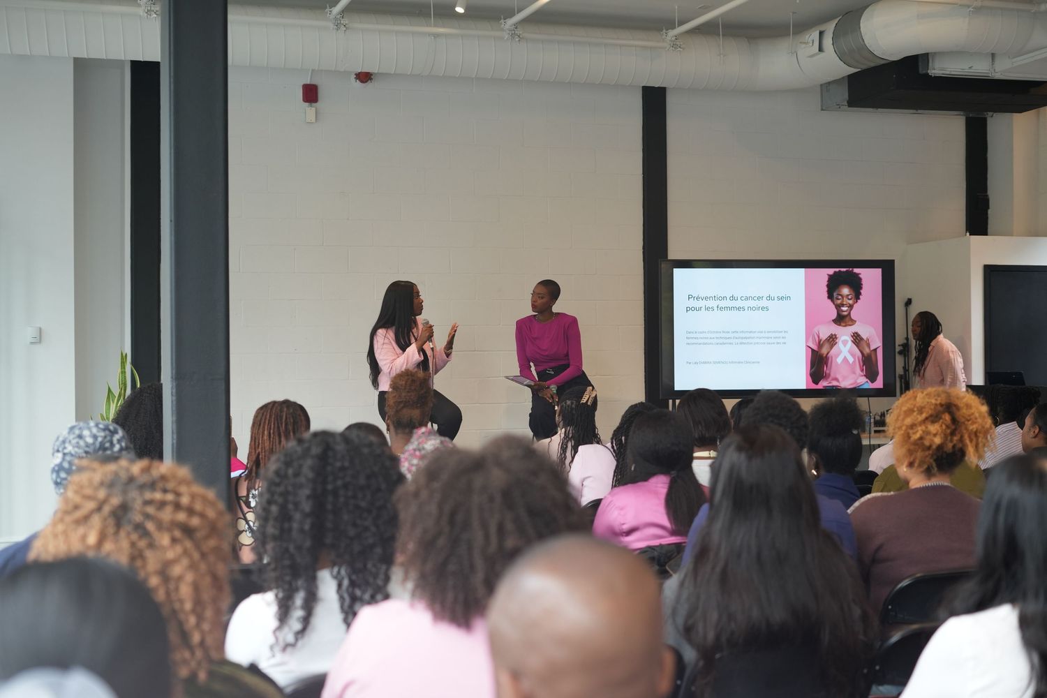A crowded conference room filled with attendees watching a presentation on a large screen at the front of the space.
