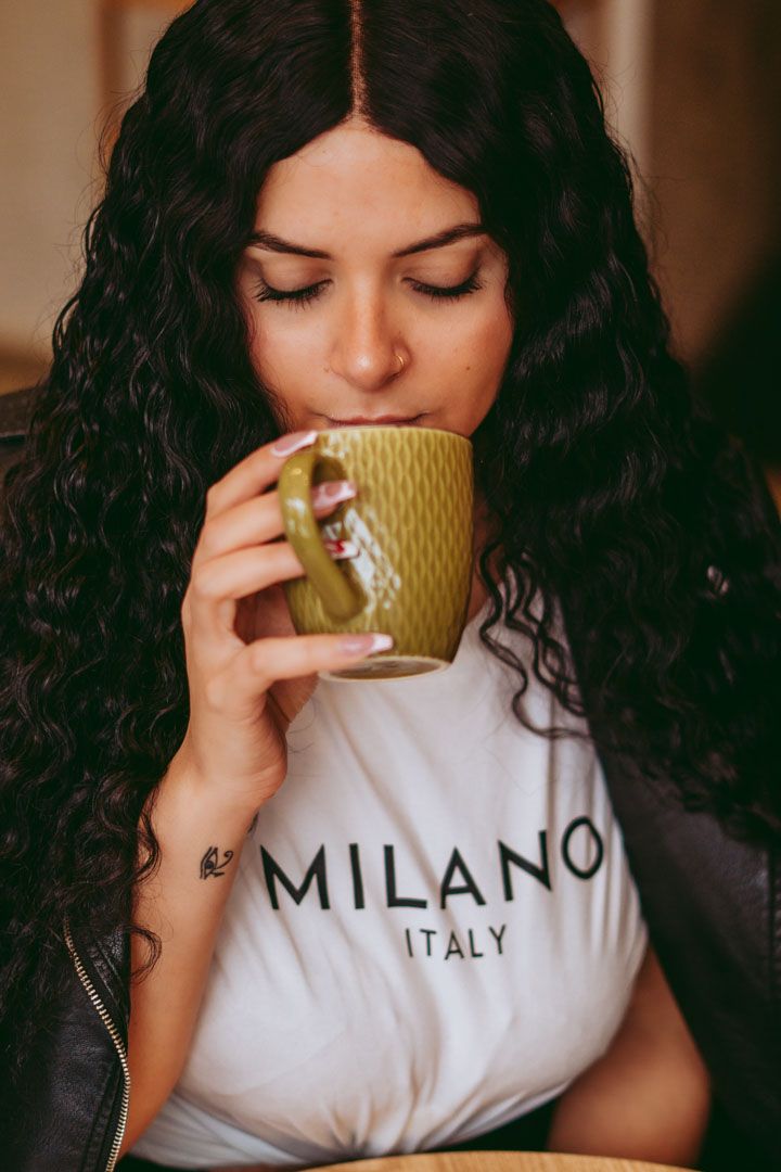 Person relaxing with yellow mug while wearing Milano t-shirt.