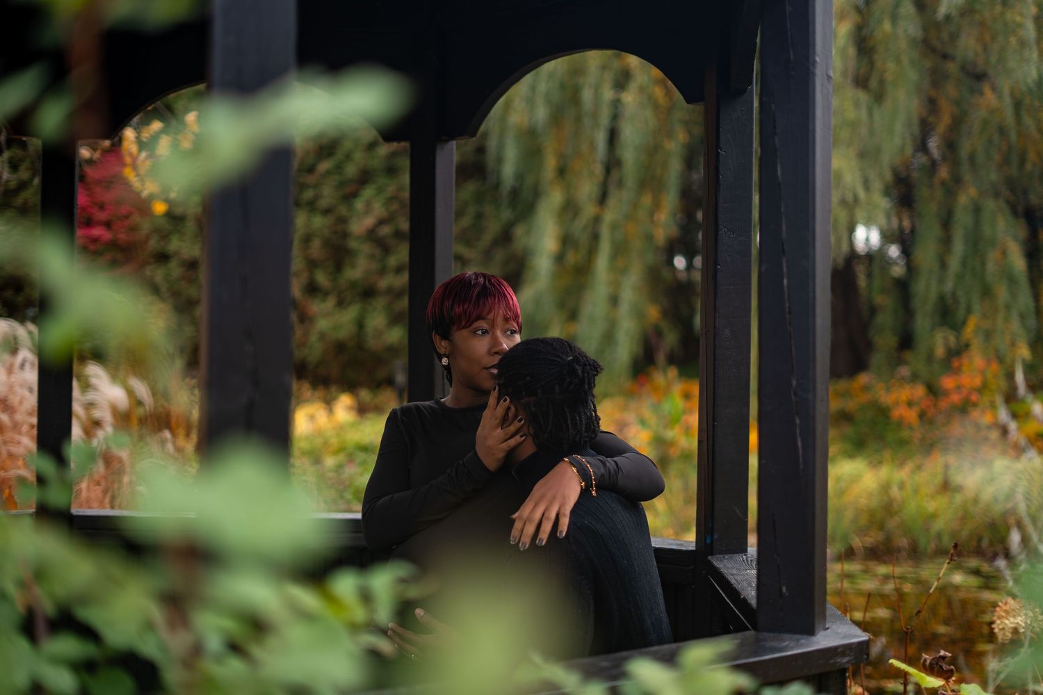 A couple shares a romantic moment under a covered gazebo in a lush garden setting during autumn.