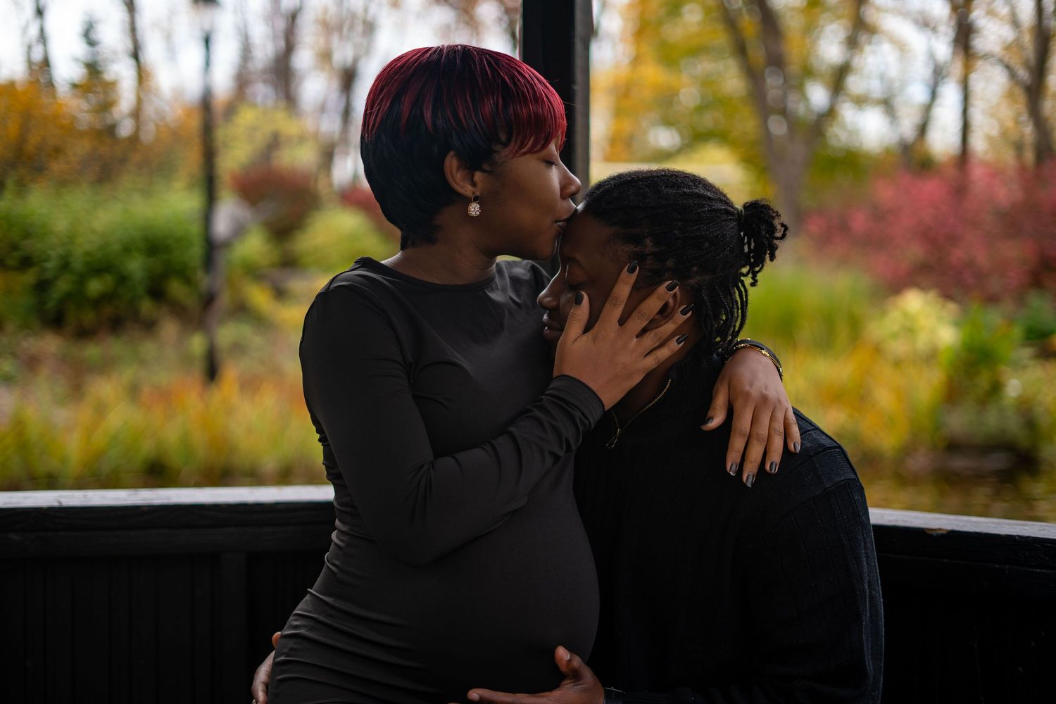 Silhouetted figures embrace intimately against an autumn backdrop with warm lighting and fall trees.
