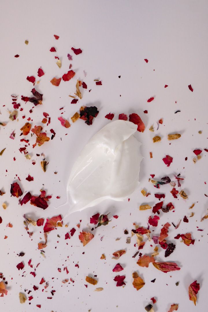 White cream texture swirled against grey background with scattered red and orange dried flower petals.