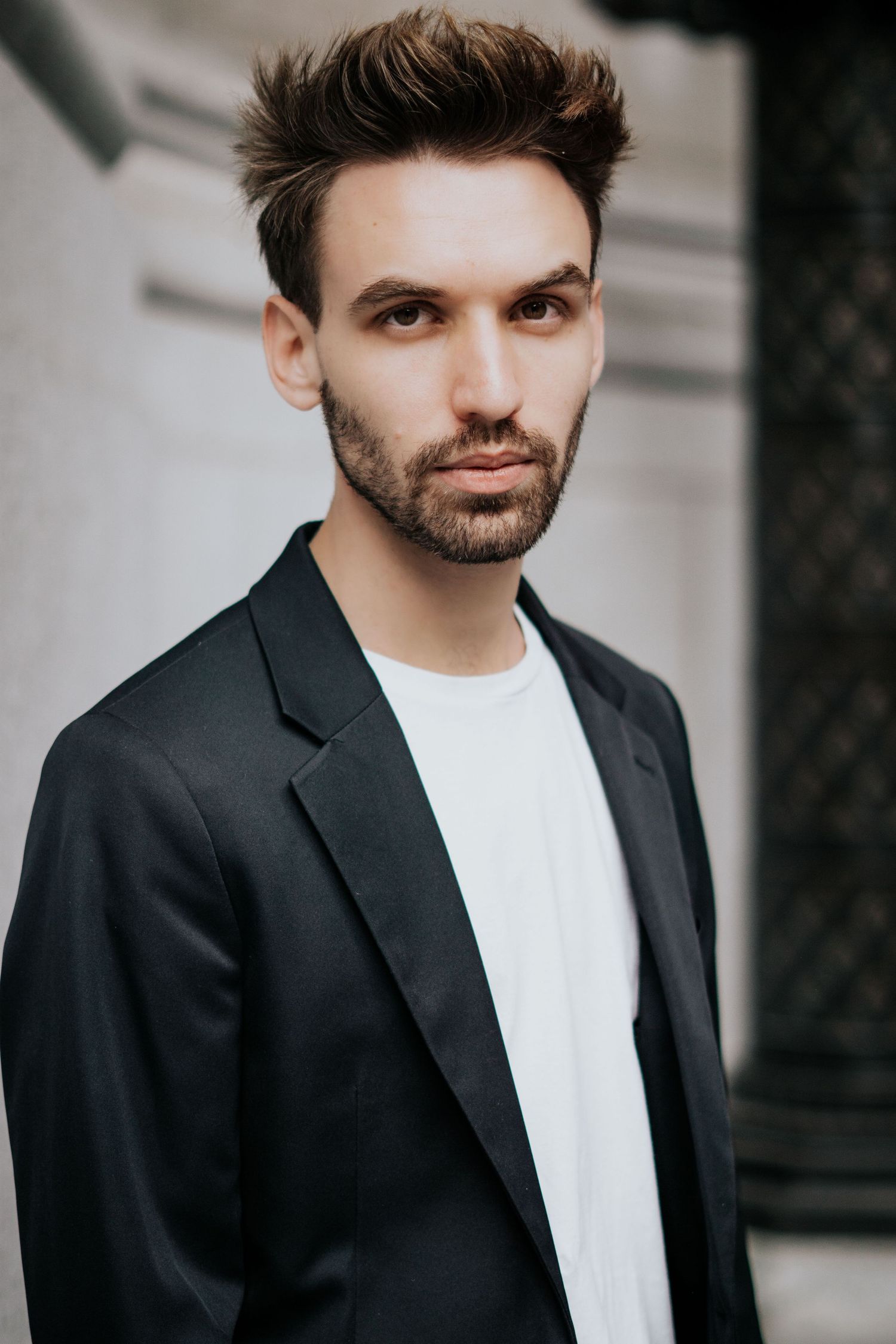 Professional portrait of someone wearing a black blazer and white t-shirt against a light background.
