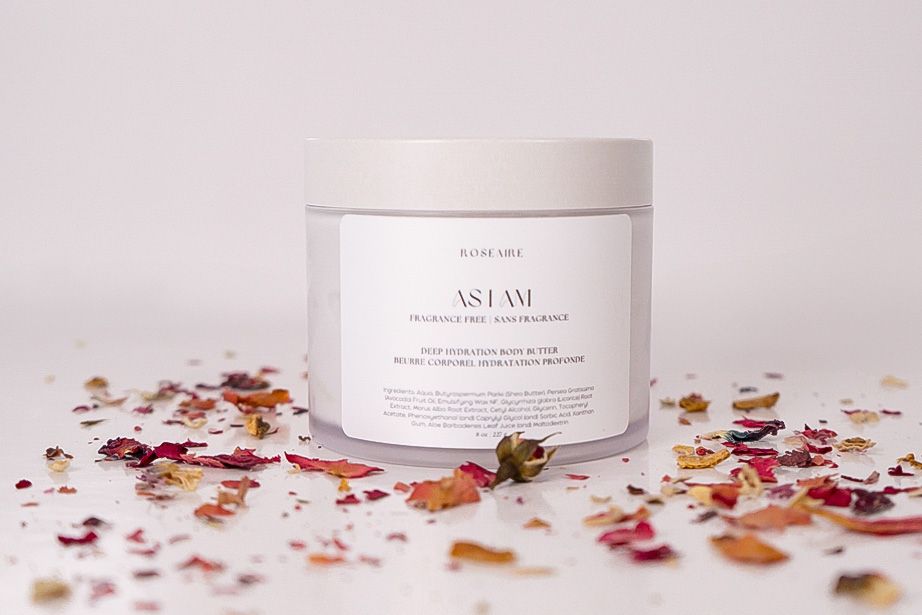 White skincare jar surrounded by scattered dried rose petals and botanicals on a light pink surface.