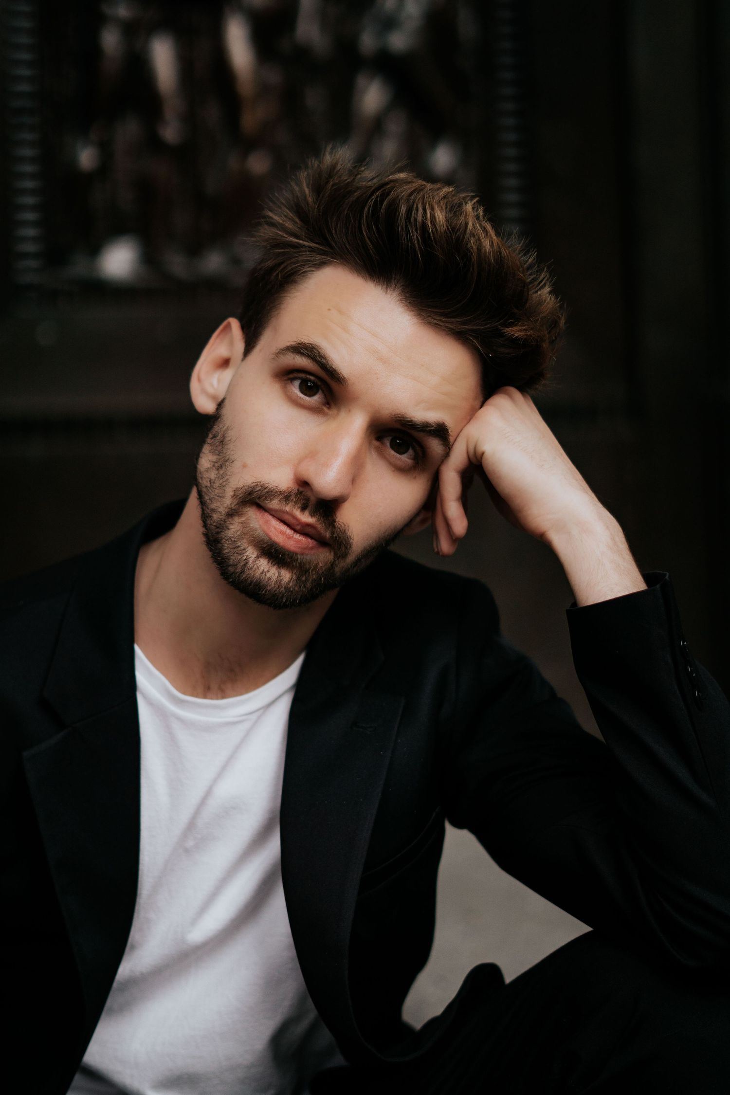 A person wearing a black blazer and white t-shirt poses against a dark background in a series of expressive portraits.