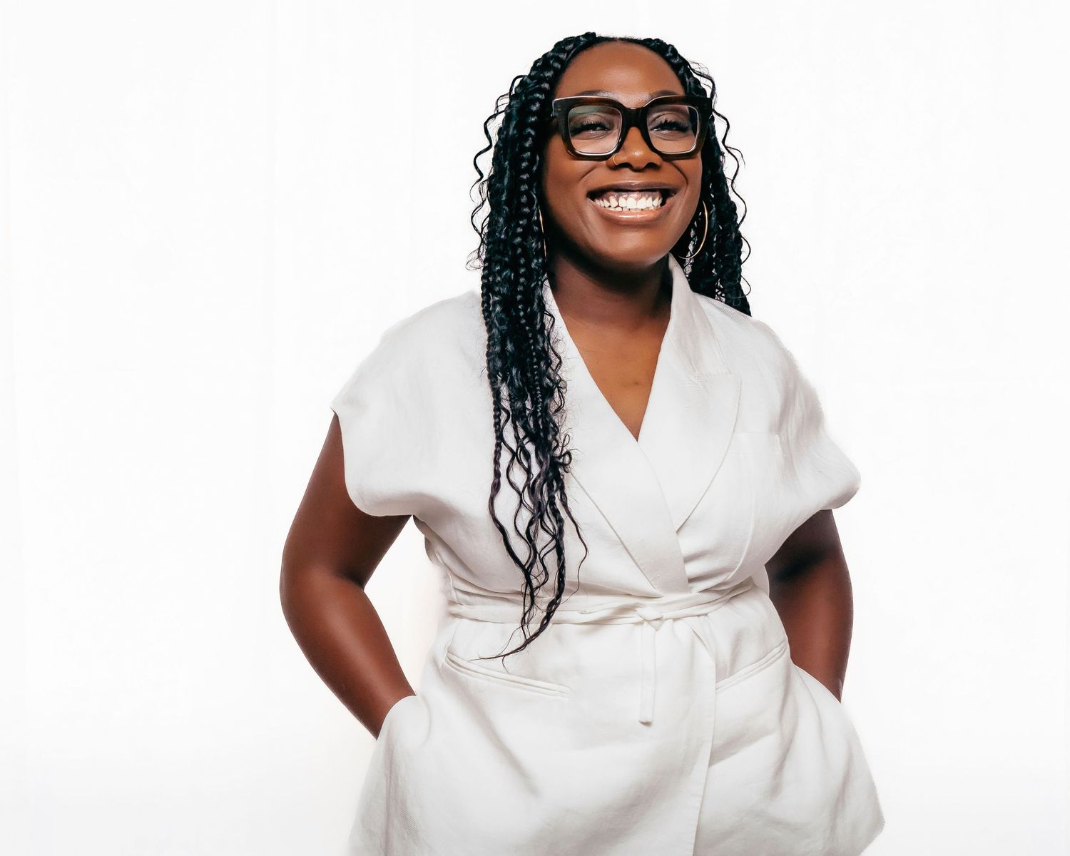 A healthcare professional in white scrubs smiles warmly while standing against a light background.