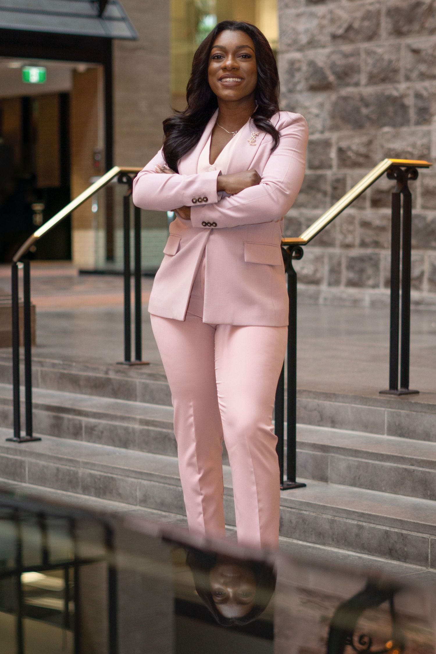 Professional model poses on stone steps wearing a stylish pink pantsuit and silver heels.