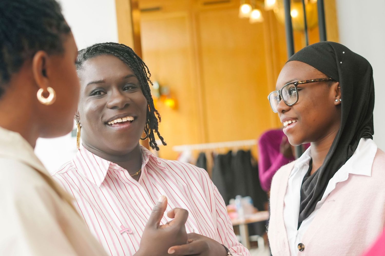 A group of people in pink and white striped shirts smile and laugh during a meeting in a bright office space.