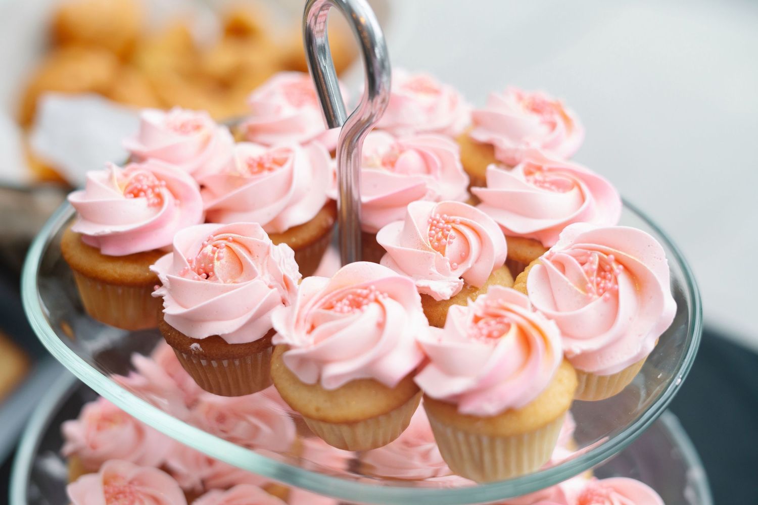 Pink frosted cupcakes arranged on a tiered glass display stand for a special occasion.
