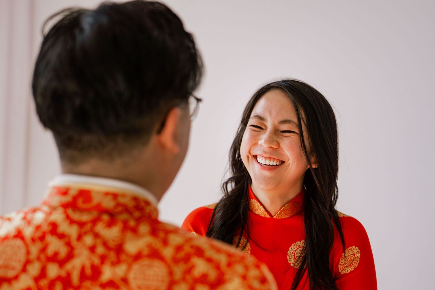 Couple in traditional Chinese wedding attire laughing together during their celebration ceremony.