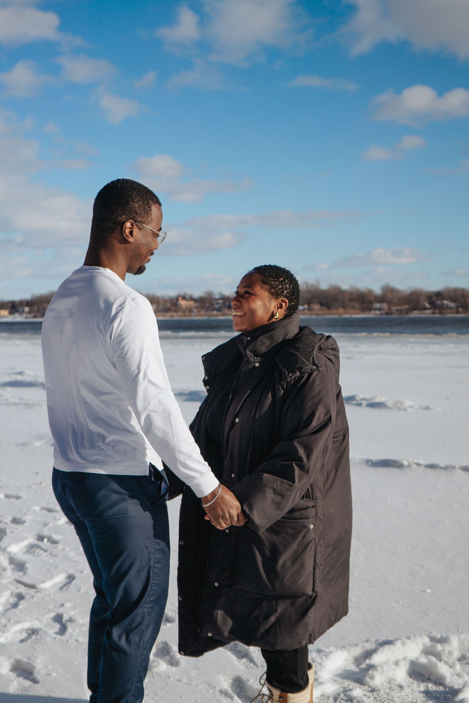 A couple holds hands while enjoying a moment together on a snowy winter day by the lake.