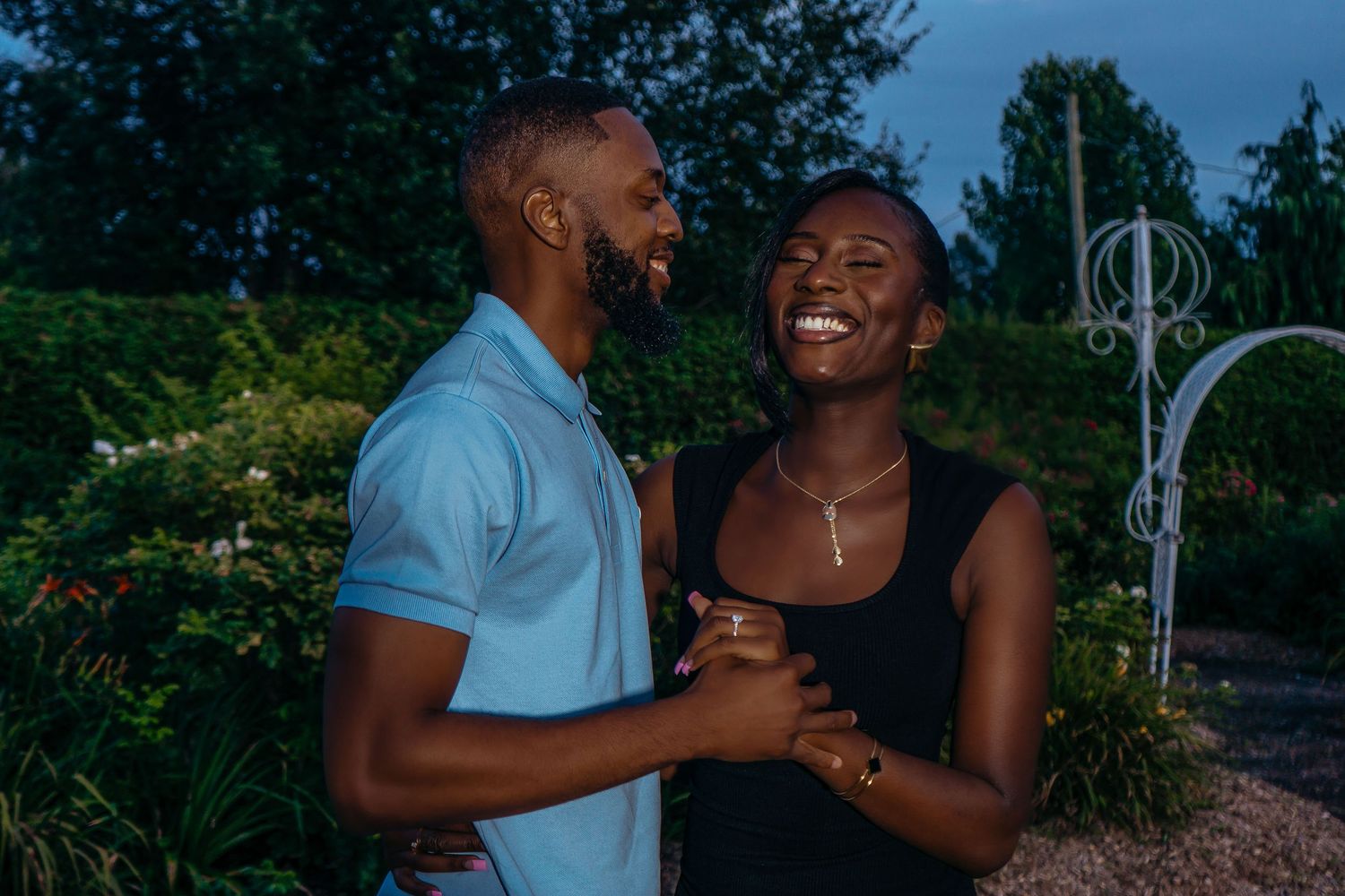 A couple shares a joyful moment together outdoors during a romantic photoshoot in a garden setting.