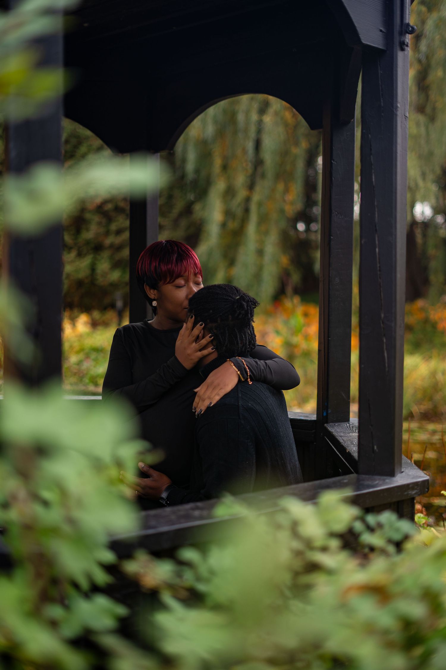 Two figures share a romantic moment in silhouette beneath a dark gazebo surrounded by autumn foliage.