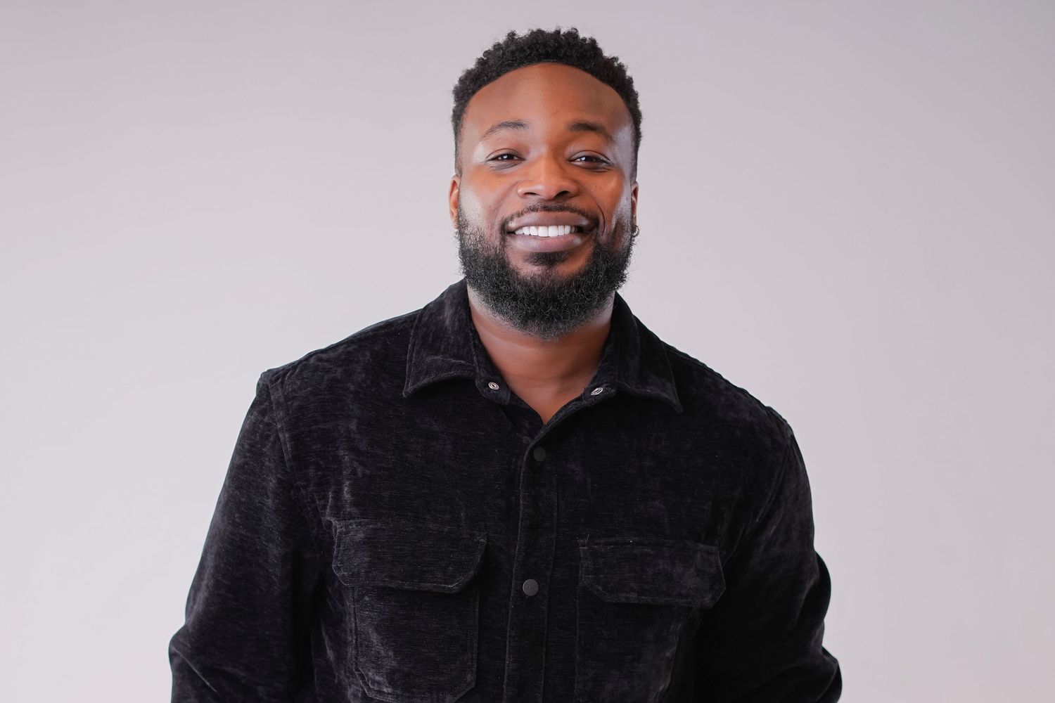 A person wearing a black jacket smiles warmly against a light gray background in a professional headshot.