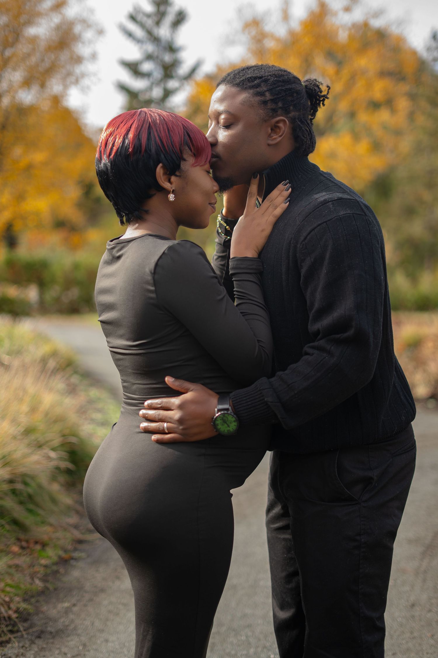 A couple shares an intimate moment outdoors during autumn with golden foliage in the background.