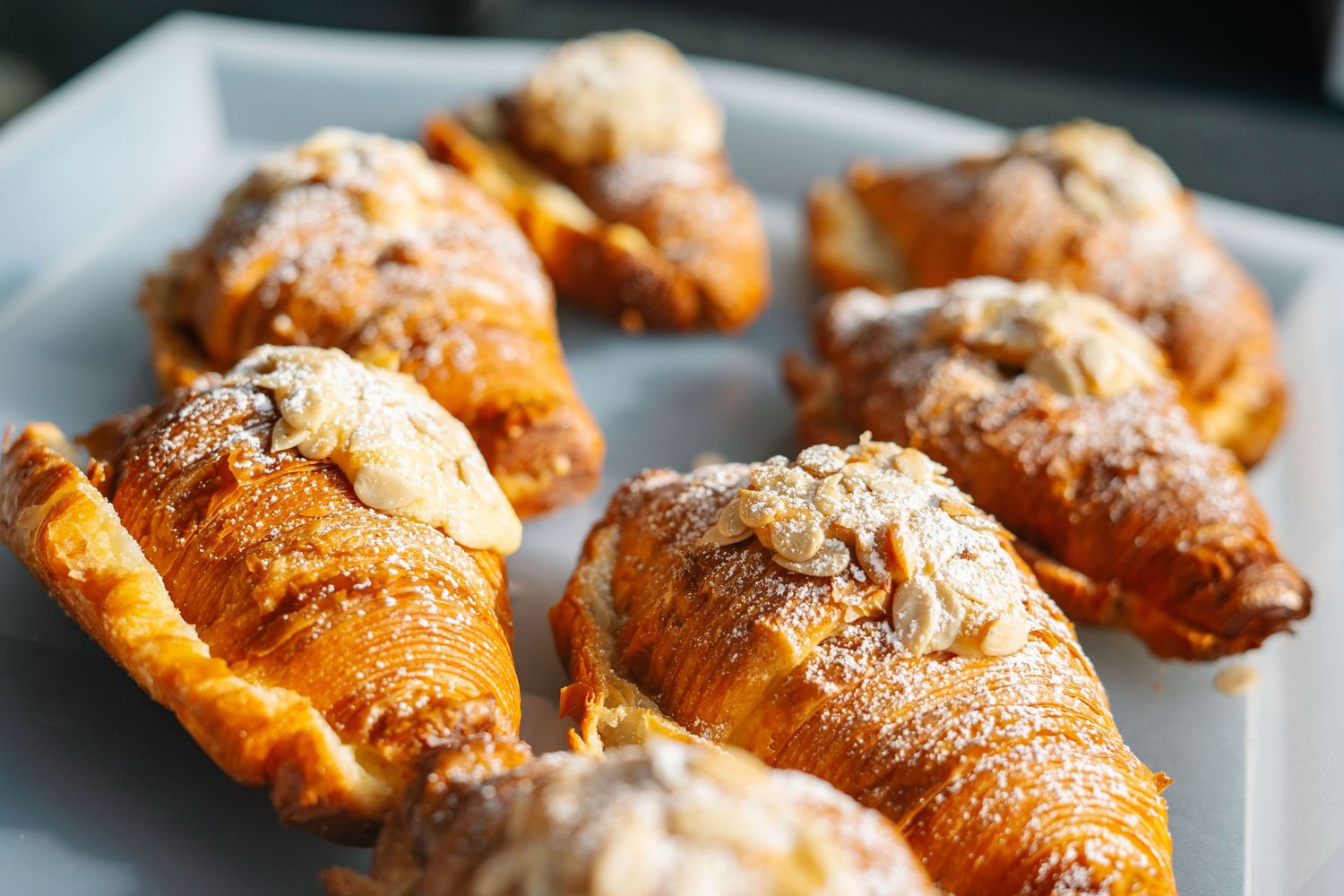 Fresh baked croissants with powdered sugar dusting arranged on a dark baking sheet.