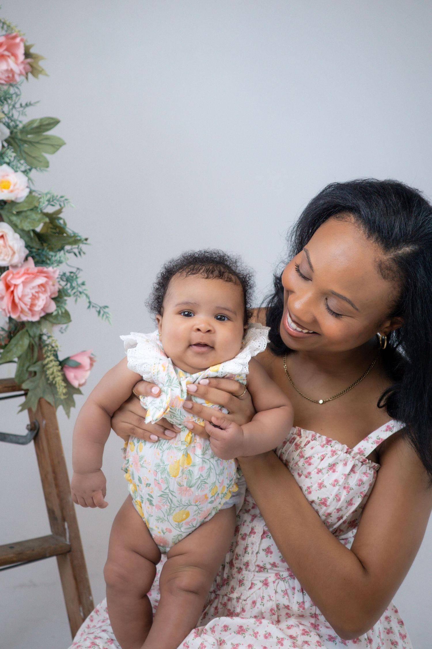 Tender interaction between mother and baby against studio backdrop with floral accents.