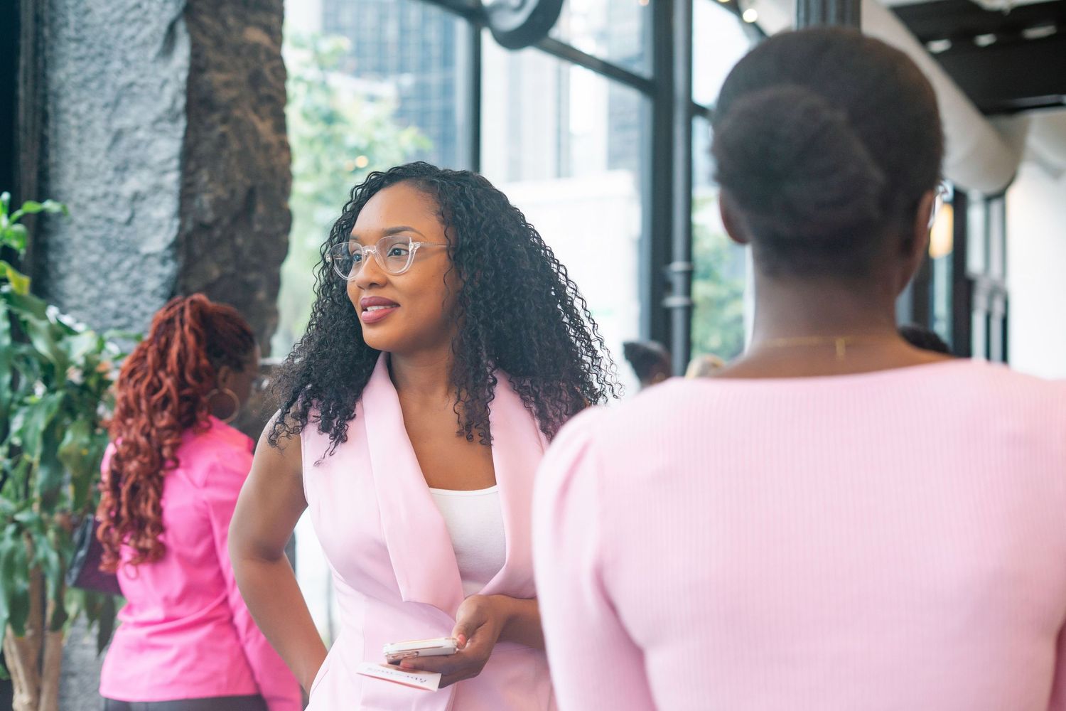 A group of people in pink and white attire gather at a bright indoor venue for a social event.